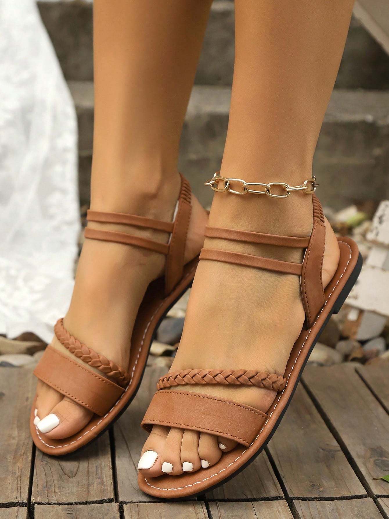 Girls brown slip-on flat Roman sandals with open toe, ankle strap, buckle and embroidery details, geometric pattern, and non-slip rubber outsole.