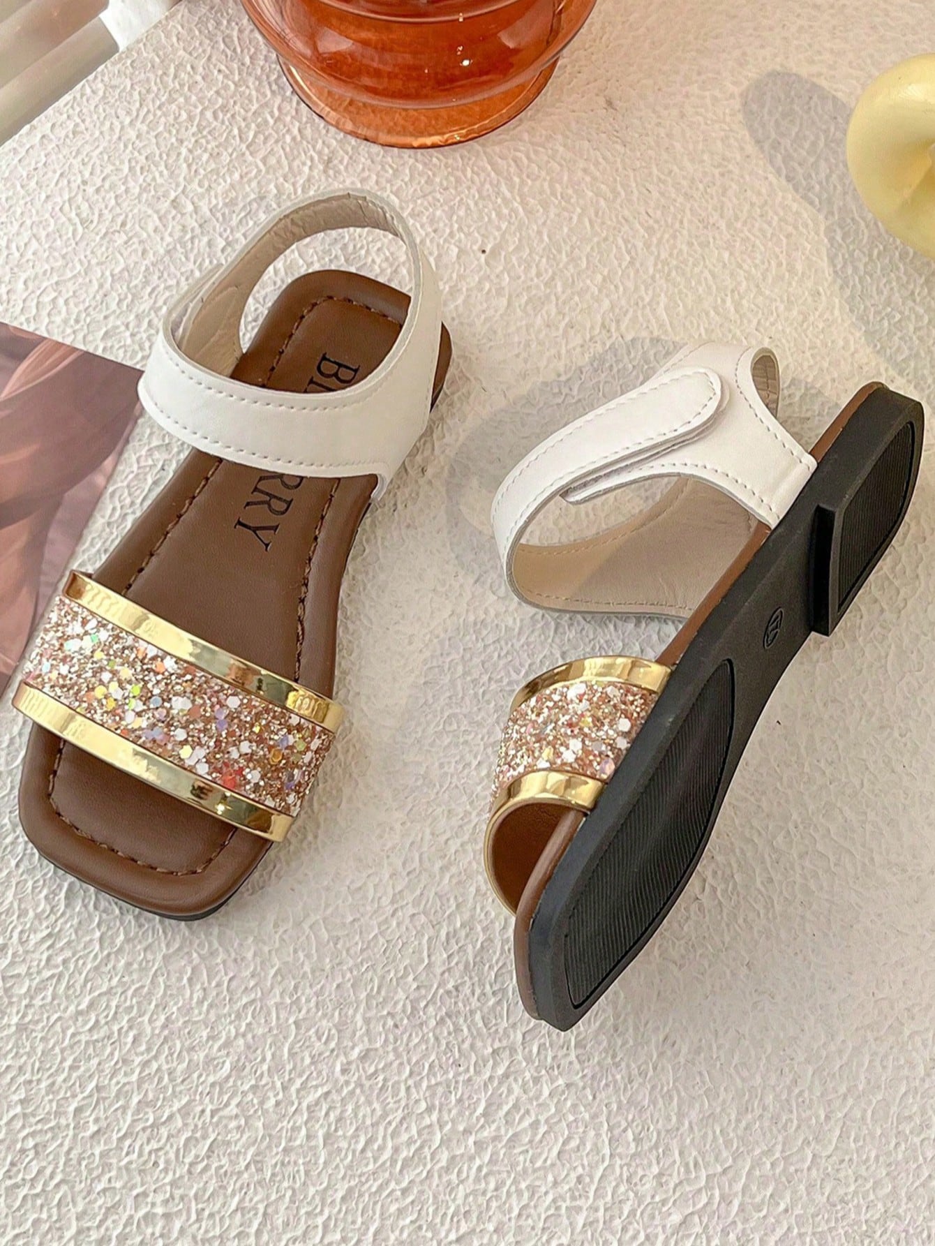 Pair of girls' pink open-toe flat sandals with ankle straps, buckle details, and a non-slip black rubber outsole.