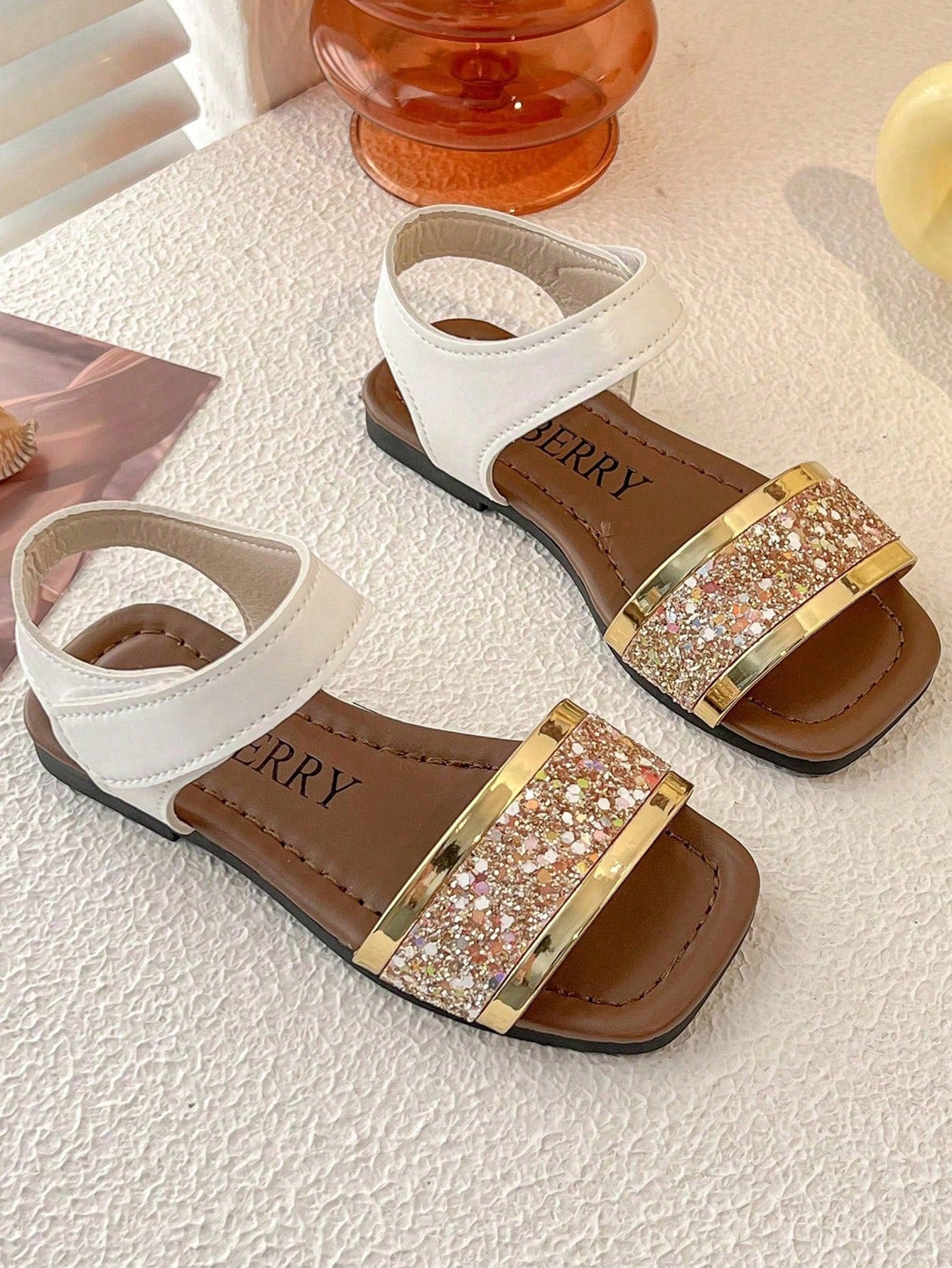 Pair of girls' pink open-toe flat sandals with ankle straps, buckle details, and a non-slip black rubber outsole.