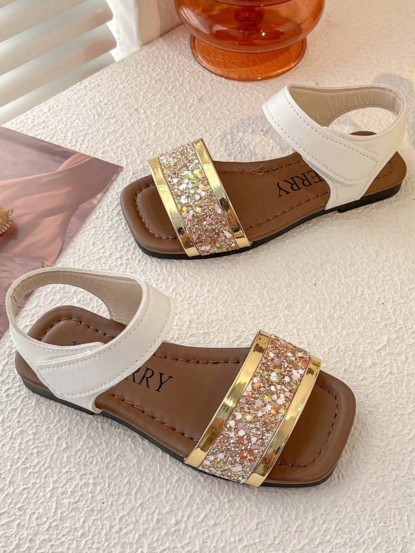 Pair of girls' pink open-toe flat sandals with ankle straps, buckle details, and a non-slip black rubber outsole.