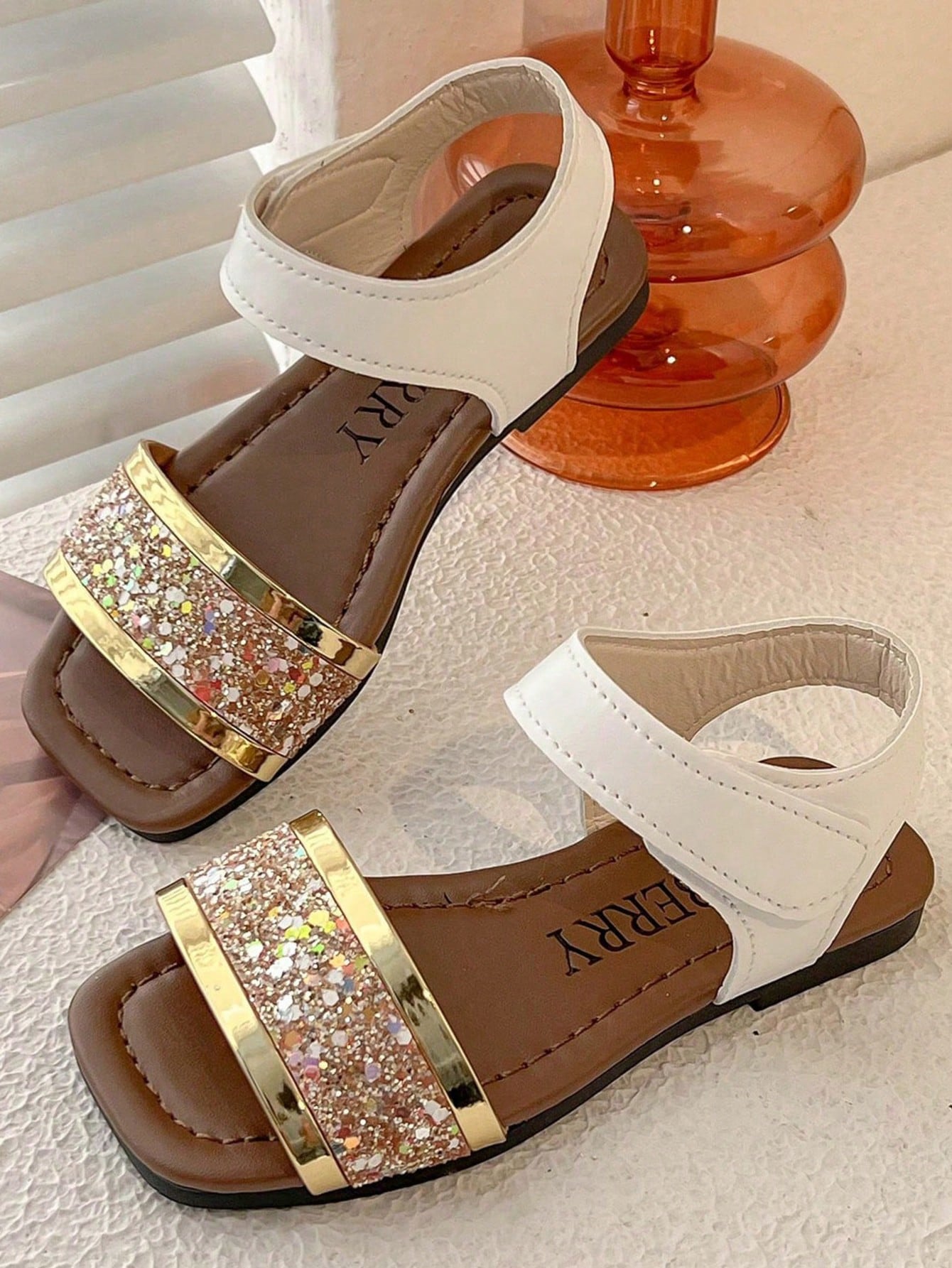 Pair of girls' pink open-toe flat sandals with ankle straps, buckle details, and a non-slip black rubber outsole.
