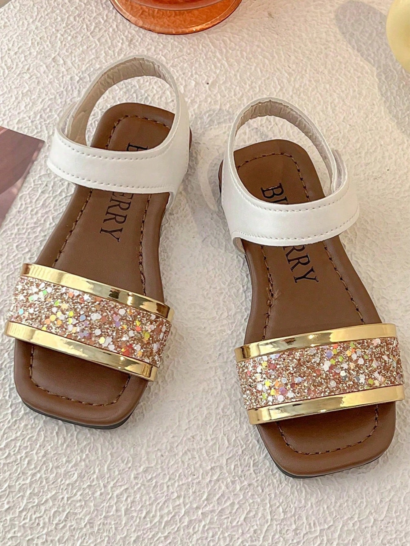 Pair of girls' pink open-toe flat sandals with ankle straps, buckle details, and a non-slip black rubber outsole.