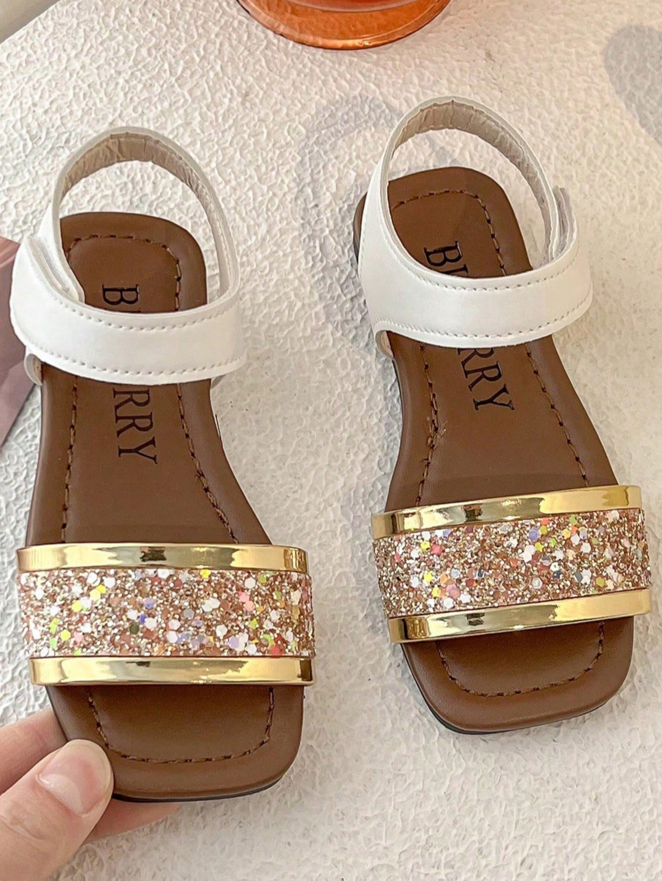 Pair of girls' pink open-toe flat sandals with ankle straps, buckle details, and a non-slip black rubber outsole.