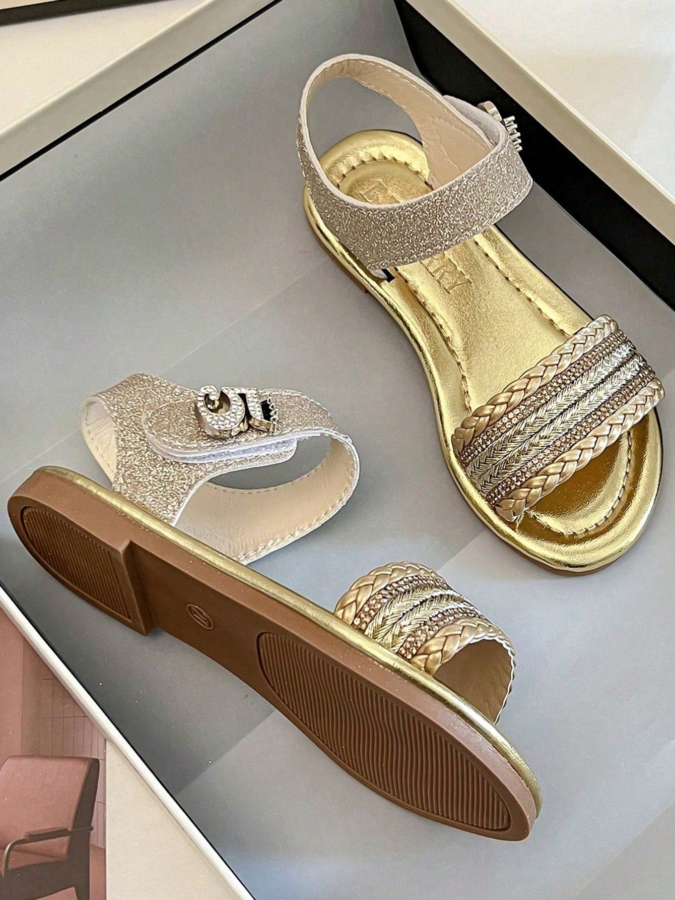 Pair of girls' pink open-toe flat sandals with ankle straps, buckle details, and a non-slip black rubber outsole.