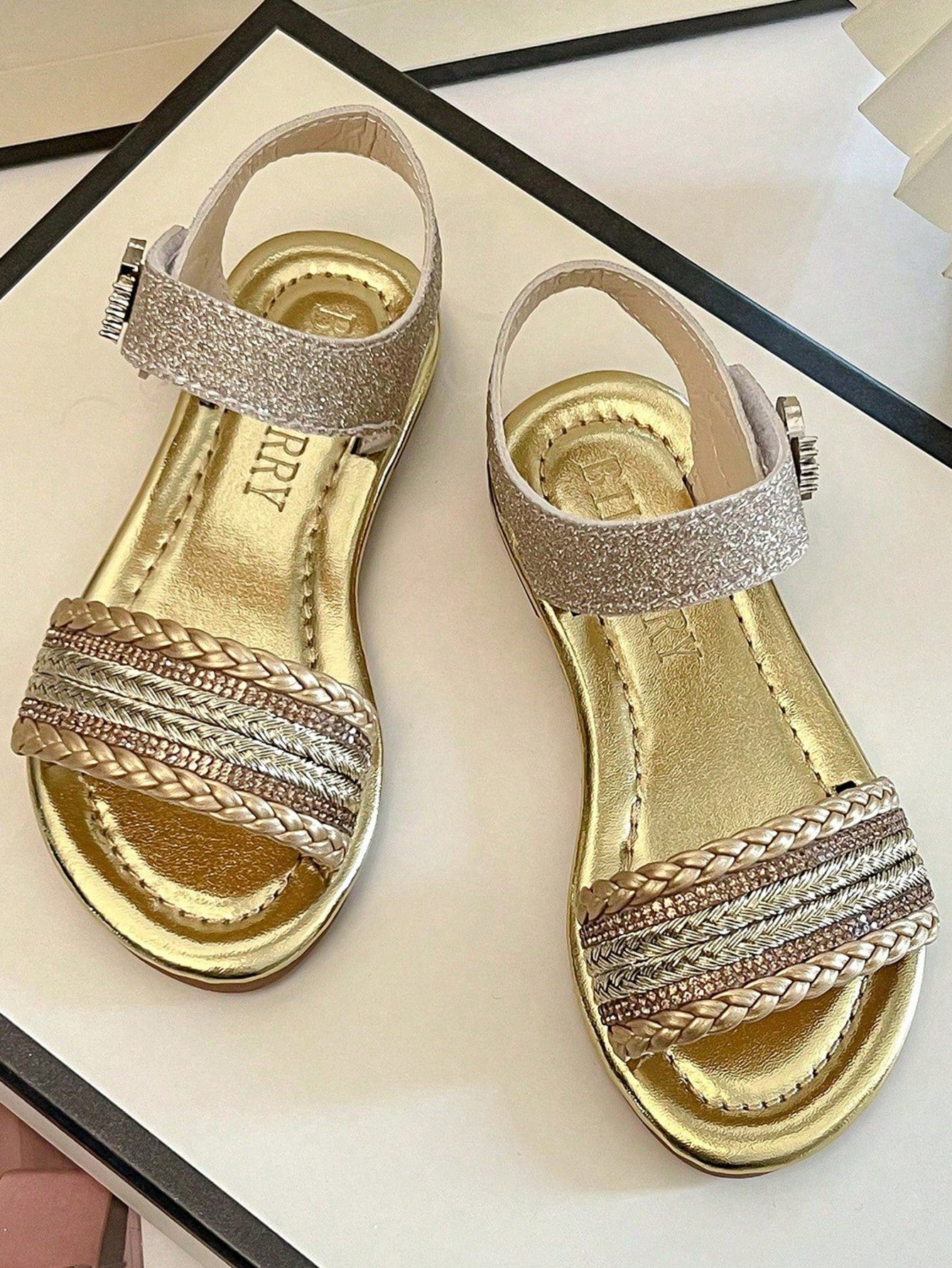 Pair of girls' pink open-toe flat sandals with ankle straps, buckle details, and a non-slip black rubber outsole.