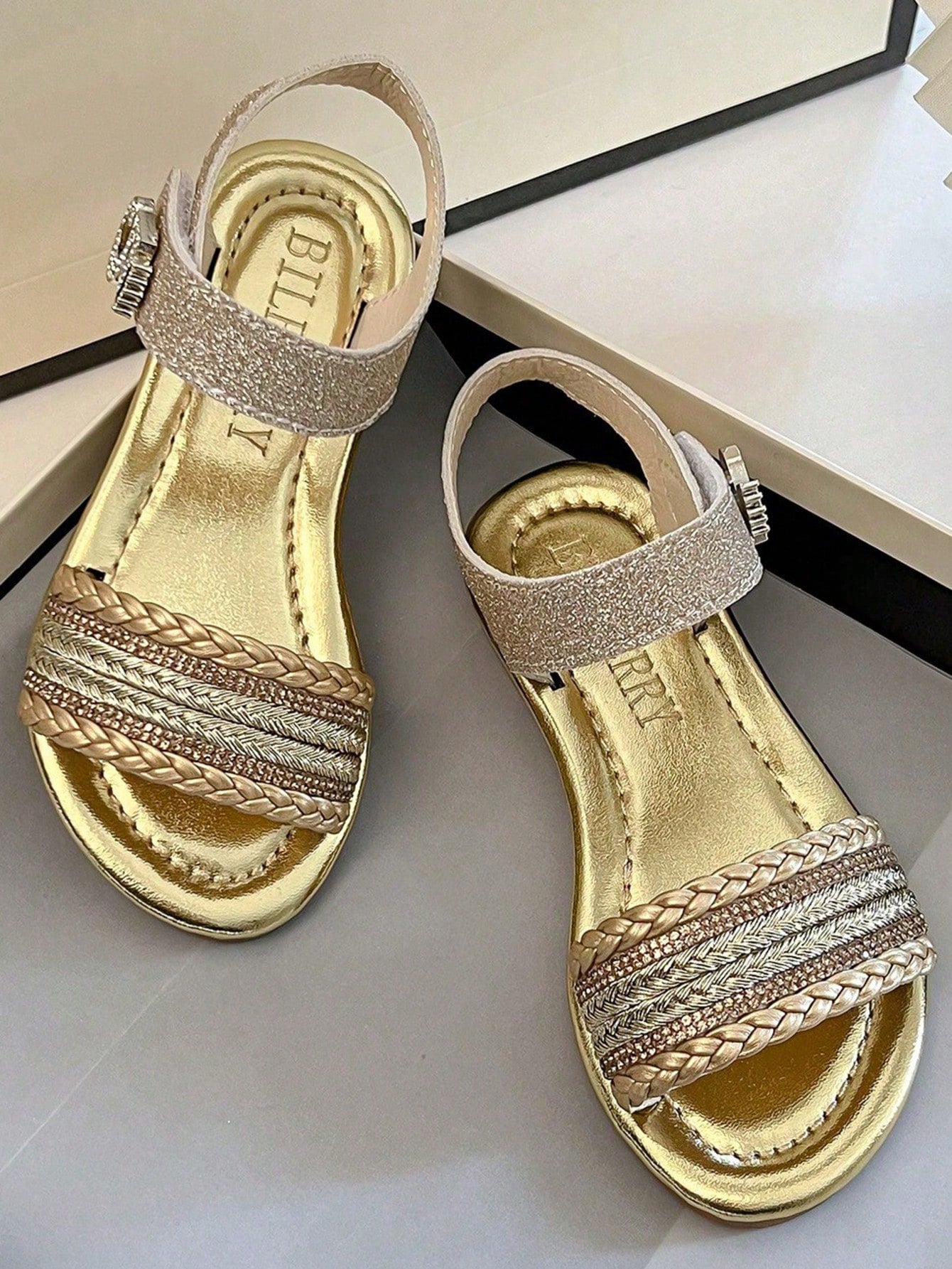 Pair of girls' pink open-toe flat sandals with ankle straps, buckle details, and a non-slip black rubber outsole.