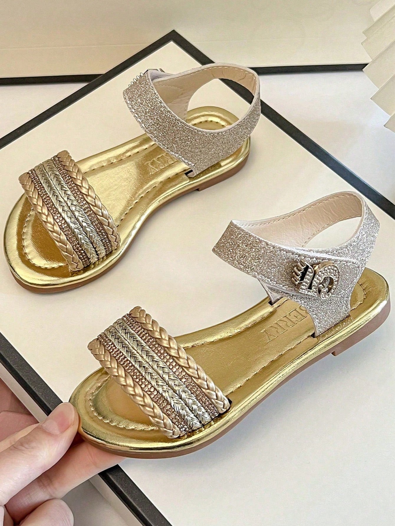 Pair of girls' pink open-toe flat sandals with ankle straps, buckle details, and a non-slip black rubber outsole.