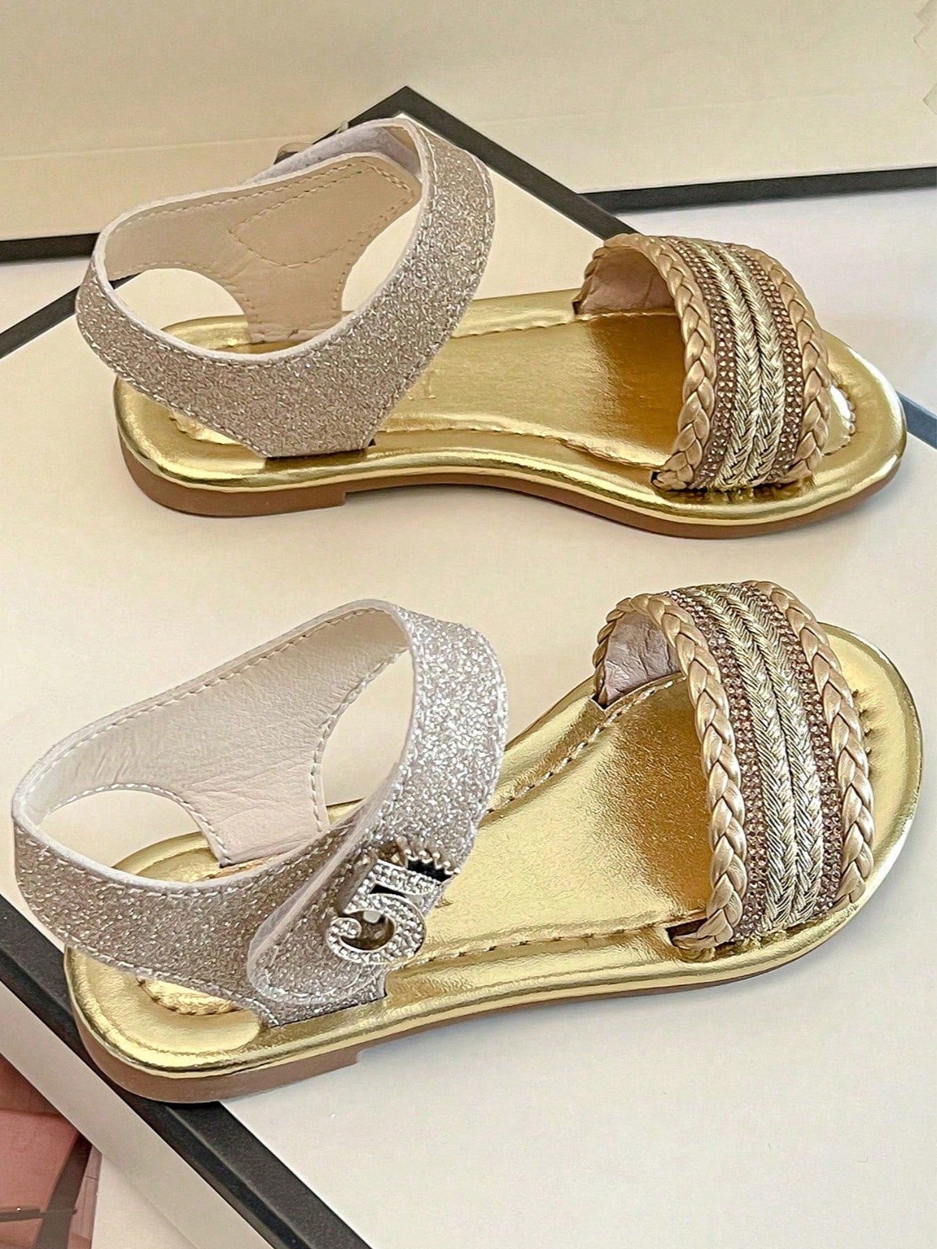Pair of girls' pink open-toe flat sandals with ankle straps, buckle details, and a non-slip black rubber outsole.