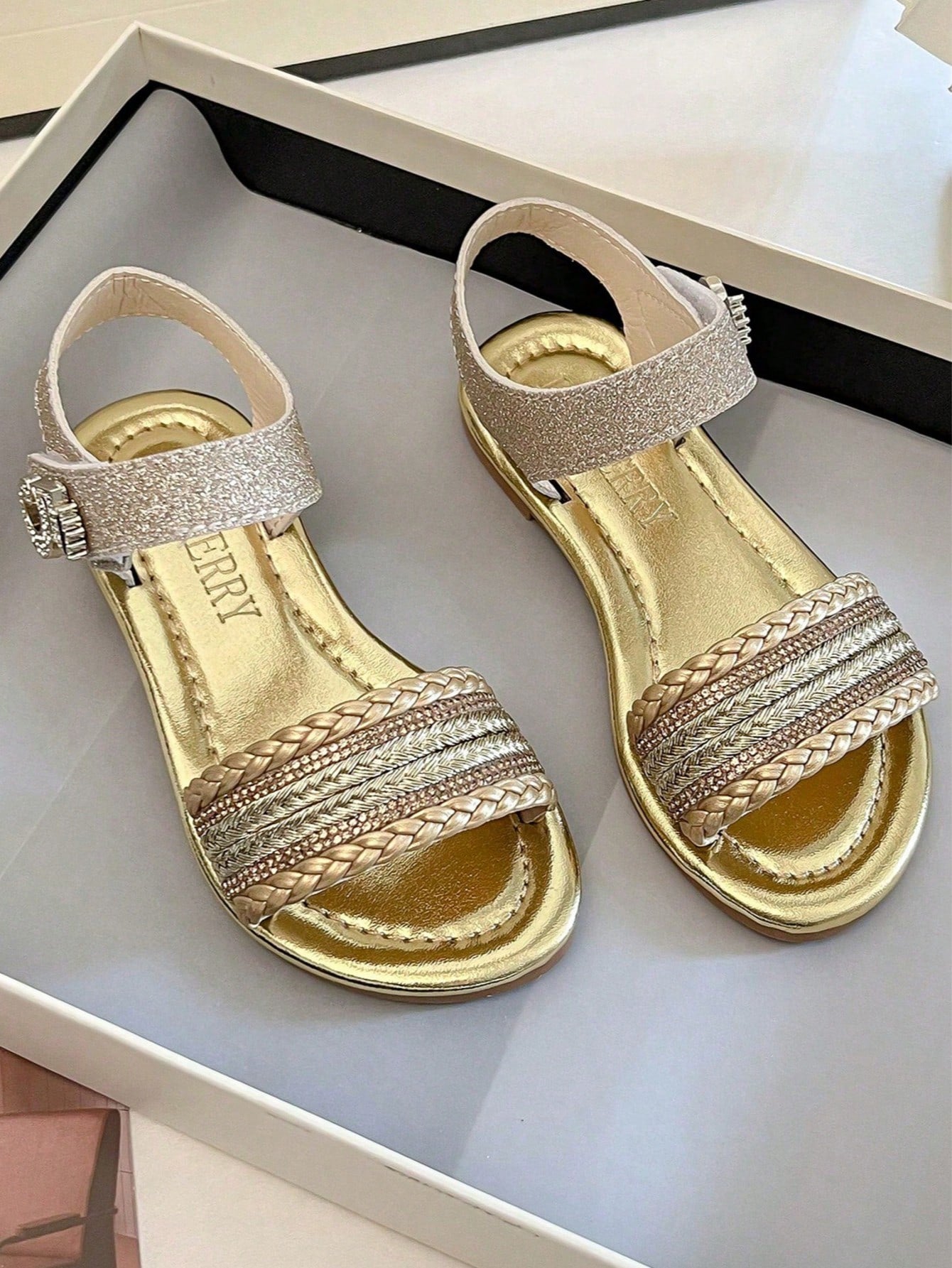 Pair of girls' pink open-toe flat sandals with ankle straps, buckle details, and a non-slip black rubber outsole.