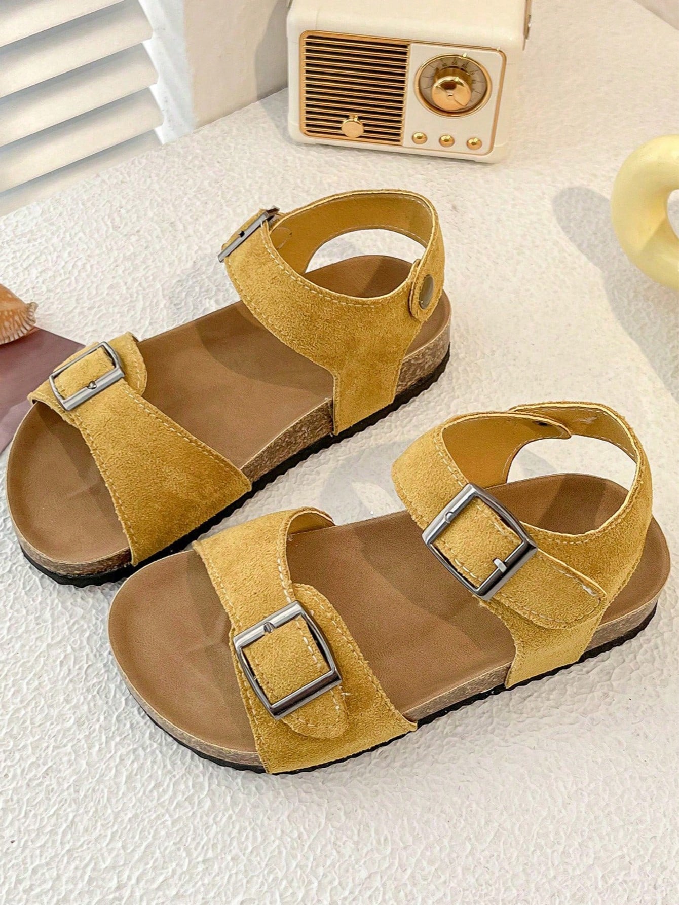 Pair of girls' pink open-toe flat sandals with ankle straps, buckle details, and a non-slip black rubber outsole.