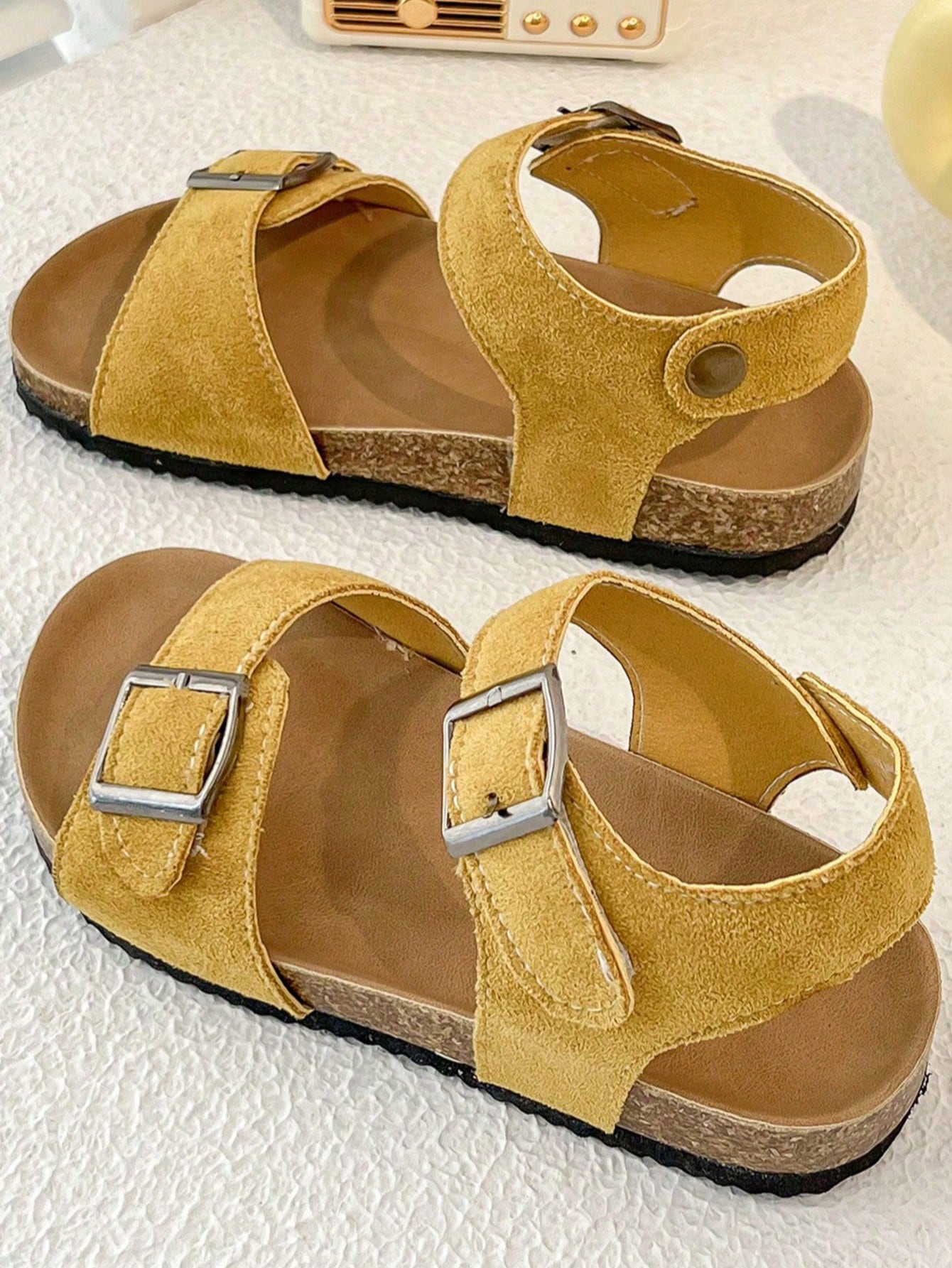 Pair of girls' pink open-toe flat sandals with ankle straps, buckle details, and a non-slip black rubber outsole.