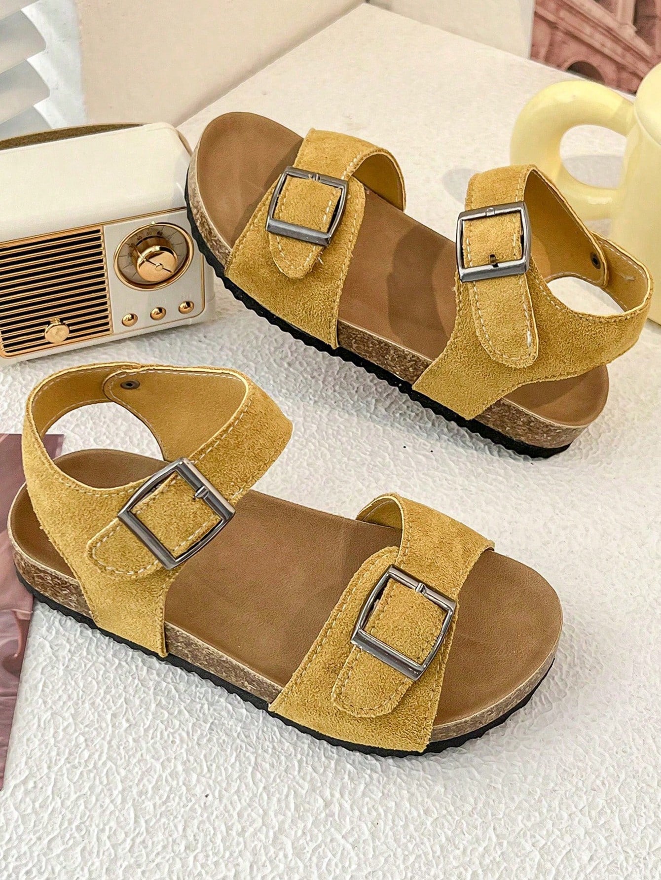 Pair of girls' pink open-toe flat sandals with ankle straps, buckle details, and a non-slip black rubber outsole.