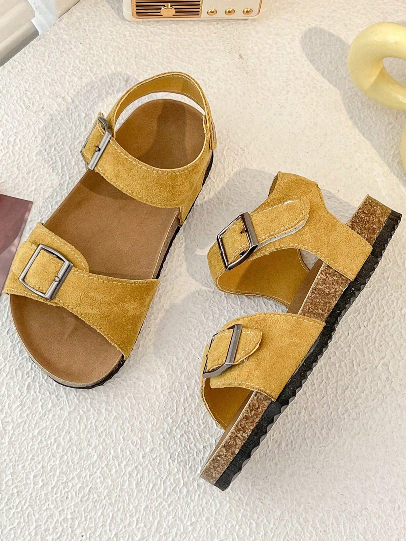 Pair of girls' pink open-toe flat sandals with ankle straps, buckle details, and a non-slip black rubber outsole.
