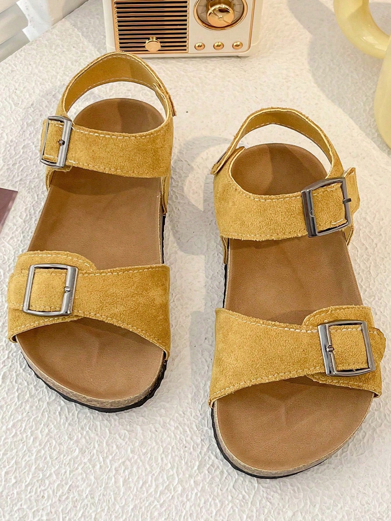 Pair of girls' pink open-toe flat sandals with ankle straps, buckle details, and a non-slip black rubber outsole.