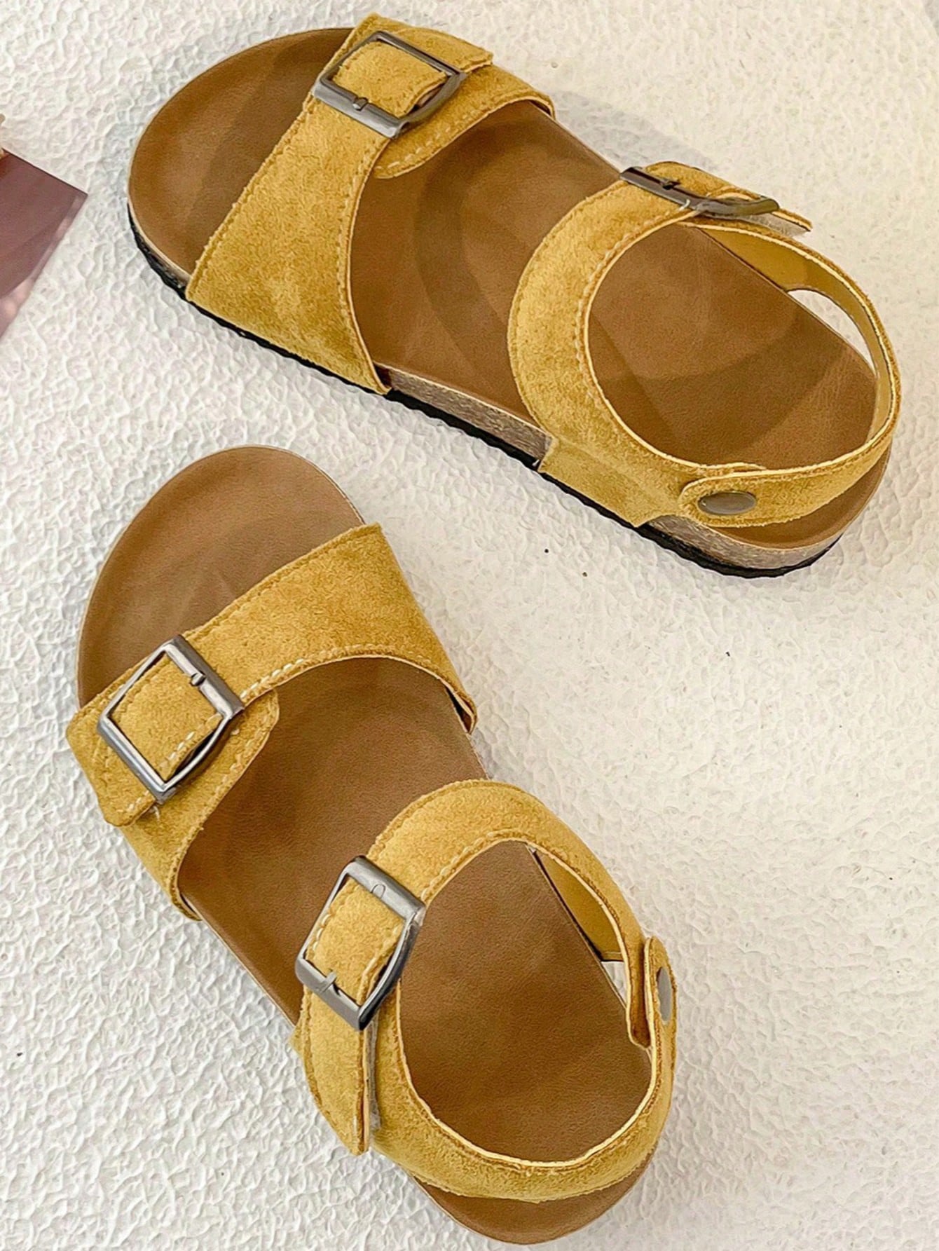 Pair of girls' pink open-toe flat sandals with ankle straps, buckle details, and a non-slip black rubber outsole.