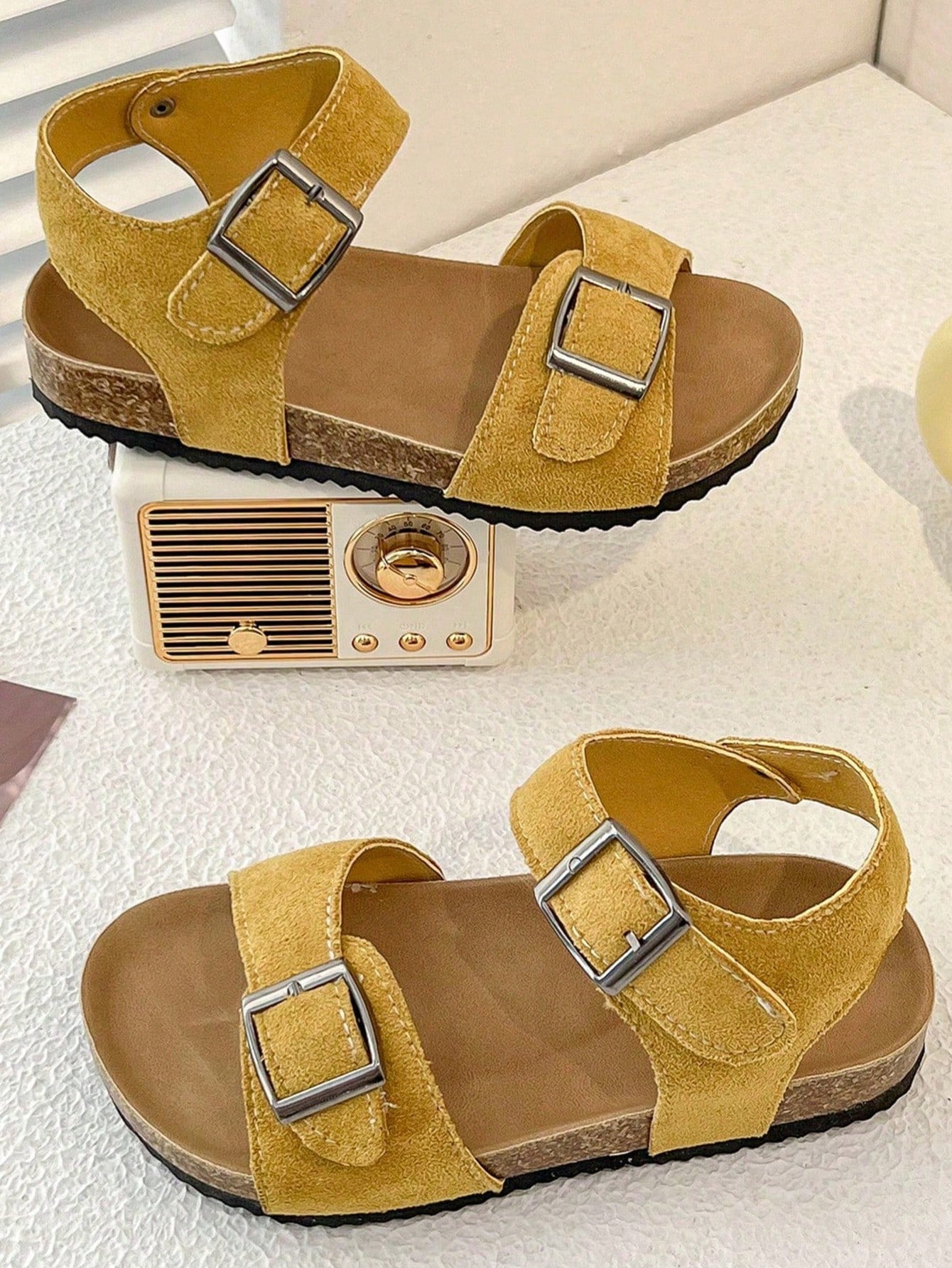 Pair of girls' pink open-toe flat sandals with ankle straps, buckle details, and a non-slip black rubber outsole.