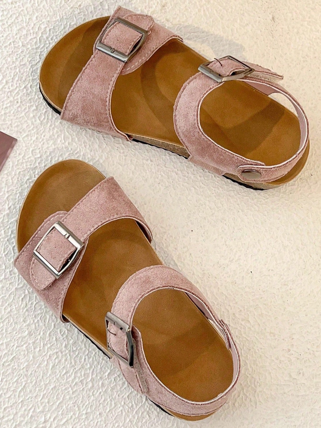 Pair of girls' pink open-toe flat sandals with ankle straps, buckle details, and a non-slip black rubber outsole.