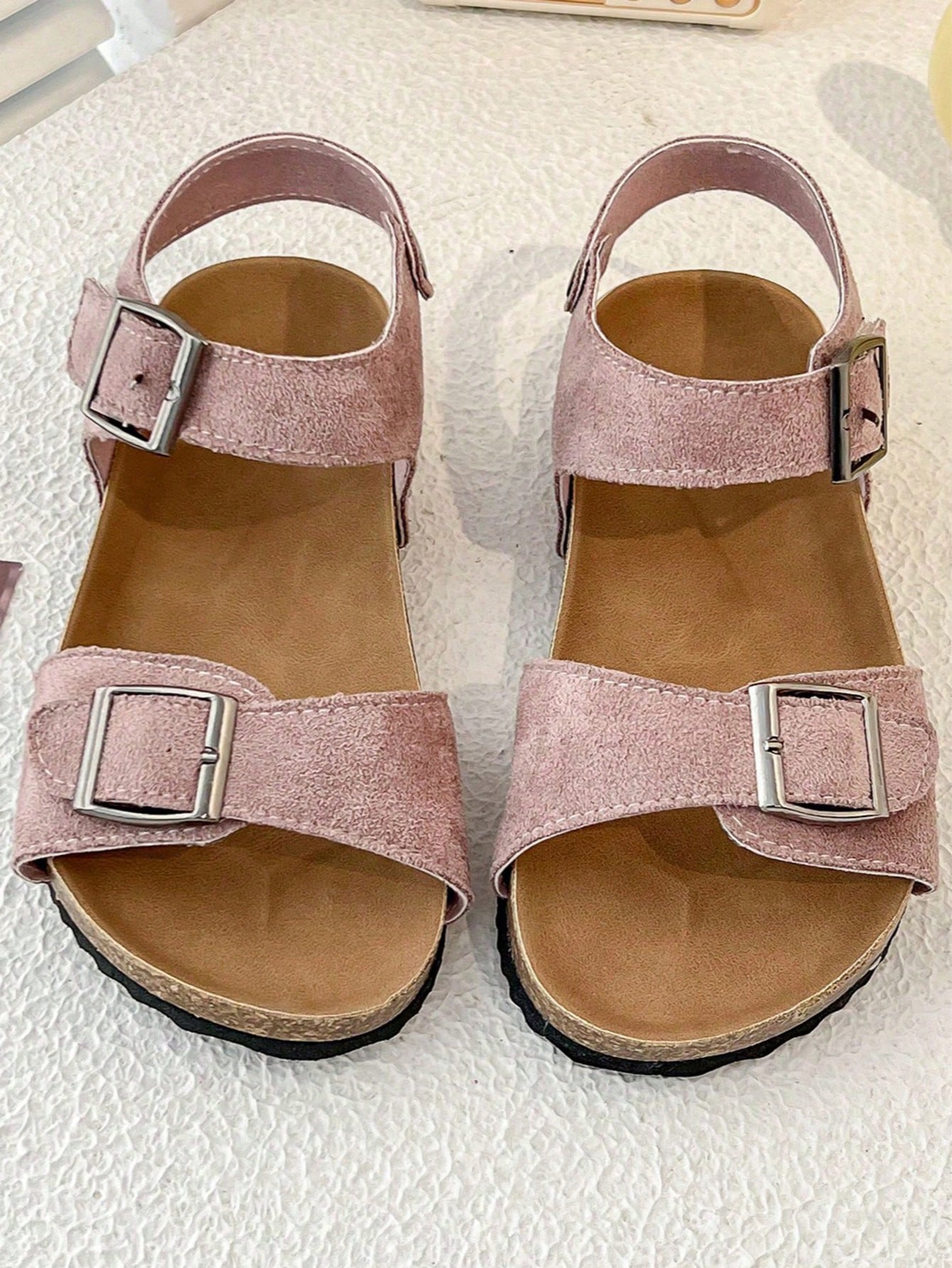 Pair of girls' pink open-toe flat sandals with ankle straps, buckle details, and a non-slip black rubber outsole.
