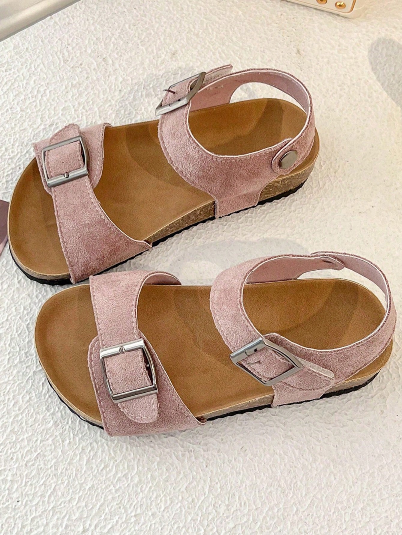 Pair of girls' pink open-toe flat sandals with ankle straps, buckle details, and a non-slip black rubber outsole.
