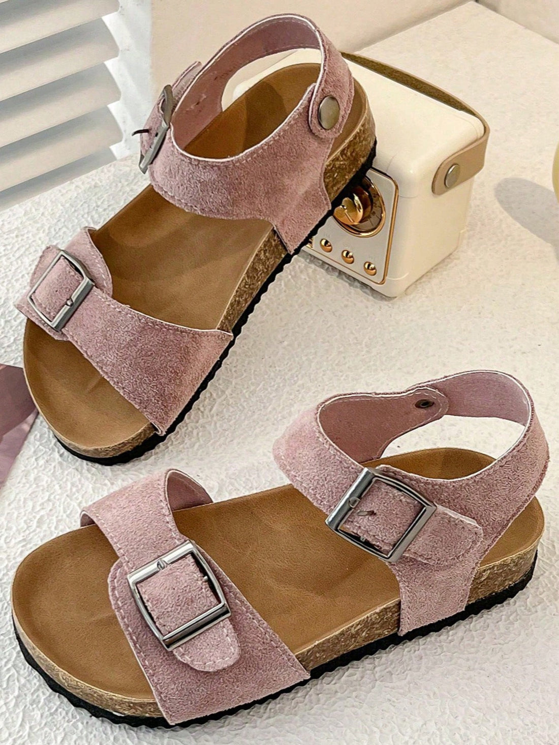 Pair of girls' pink open-toe flat sandals with ankle straps, buckle details, and a non-slip black rubber outsole.