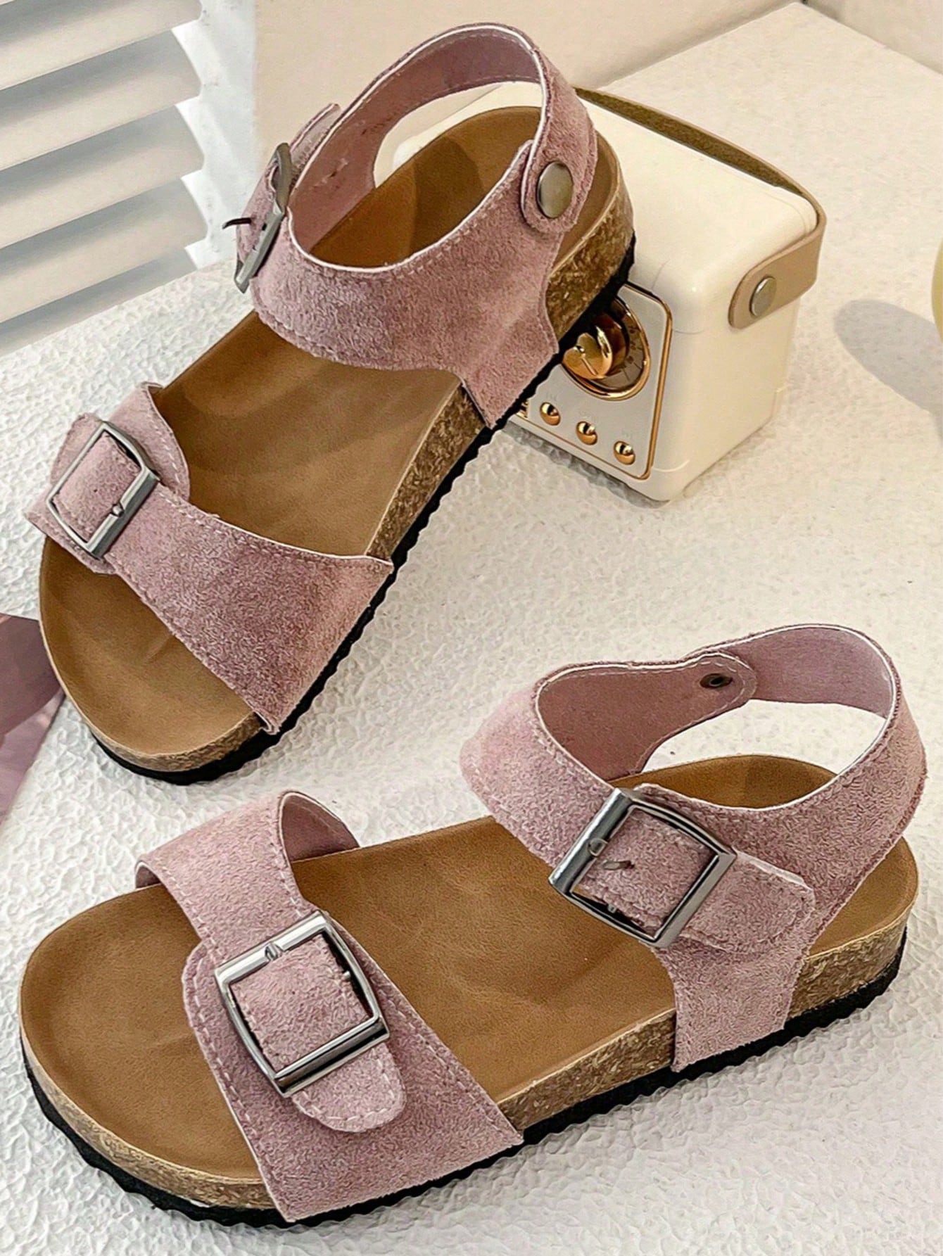 Pair of girls' pink open-toe flat sandals with ankle straps, buckle details, and a non-slip black rubber outsole.