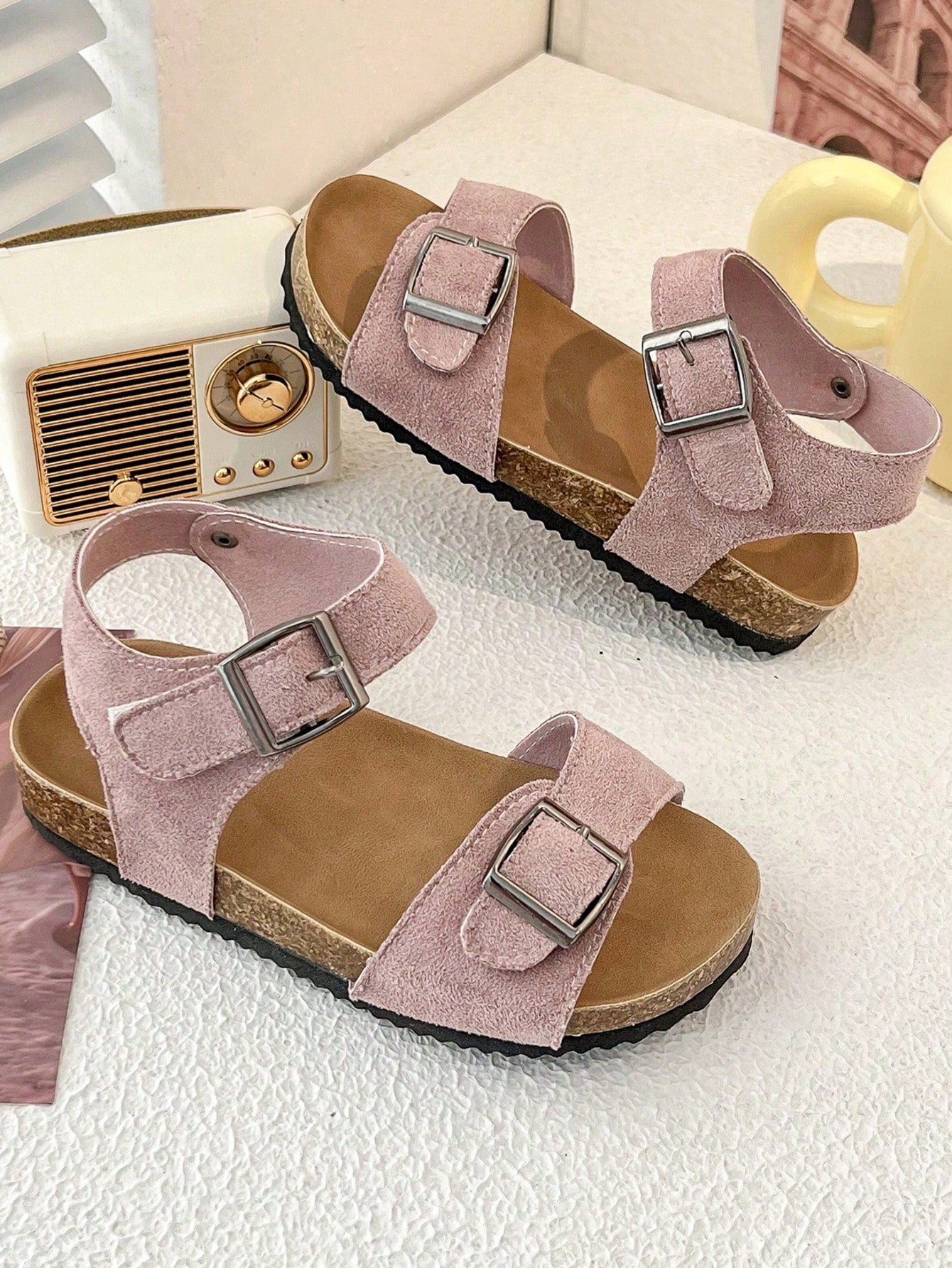 Pair of girls' pink open-toe flat sandals with ankle straps, buckle details, and a non-slip black rubber outsole.