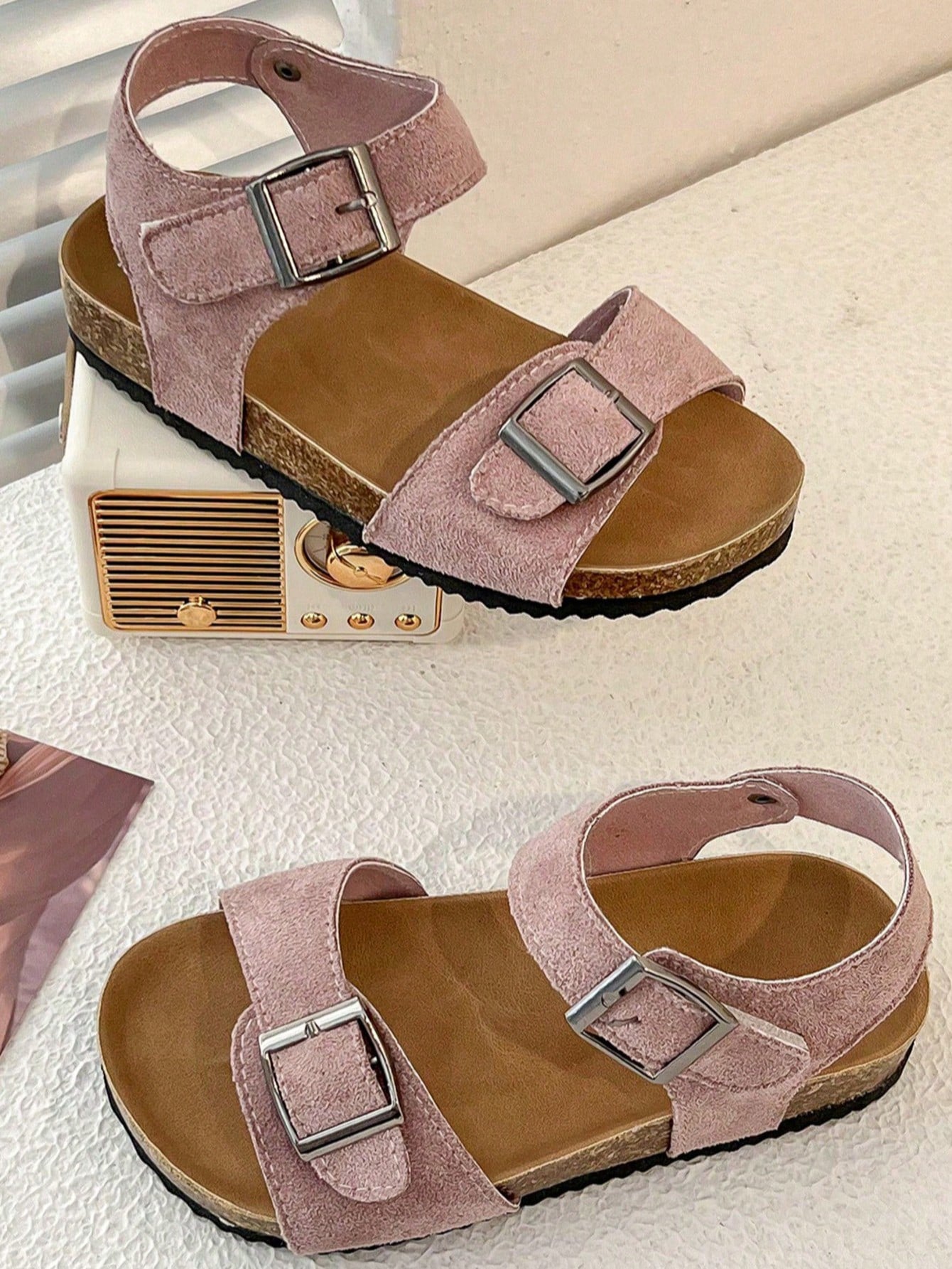 Pair of girls' pink open-toe flat sandals with ankle straps, buckle details, and a non-slip black rubber outsole.