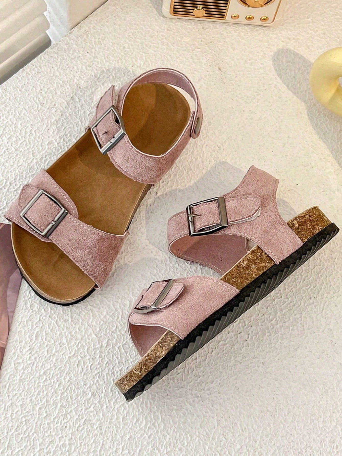 Pair of girls' pink open-toe flat sandals with ankle straps, buckle details, and a non-slip black rubber outsole.