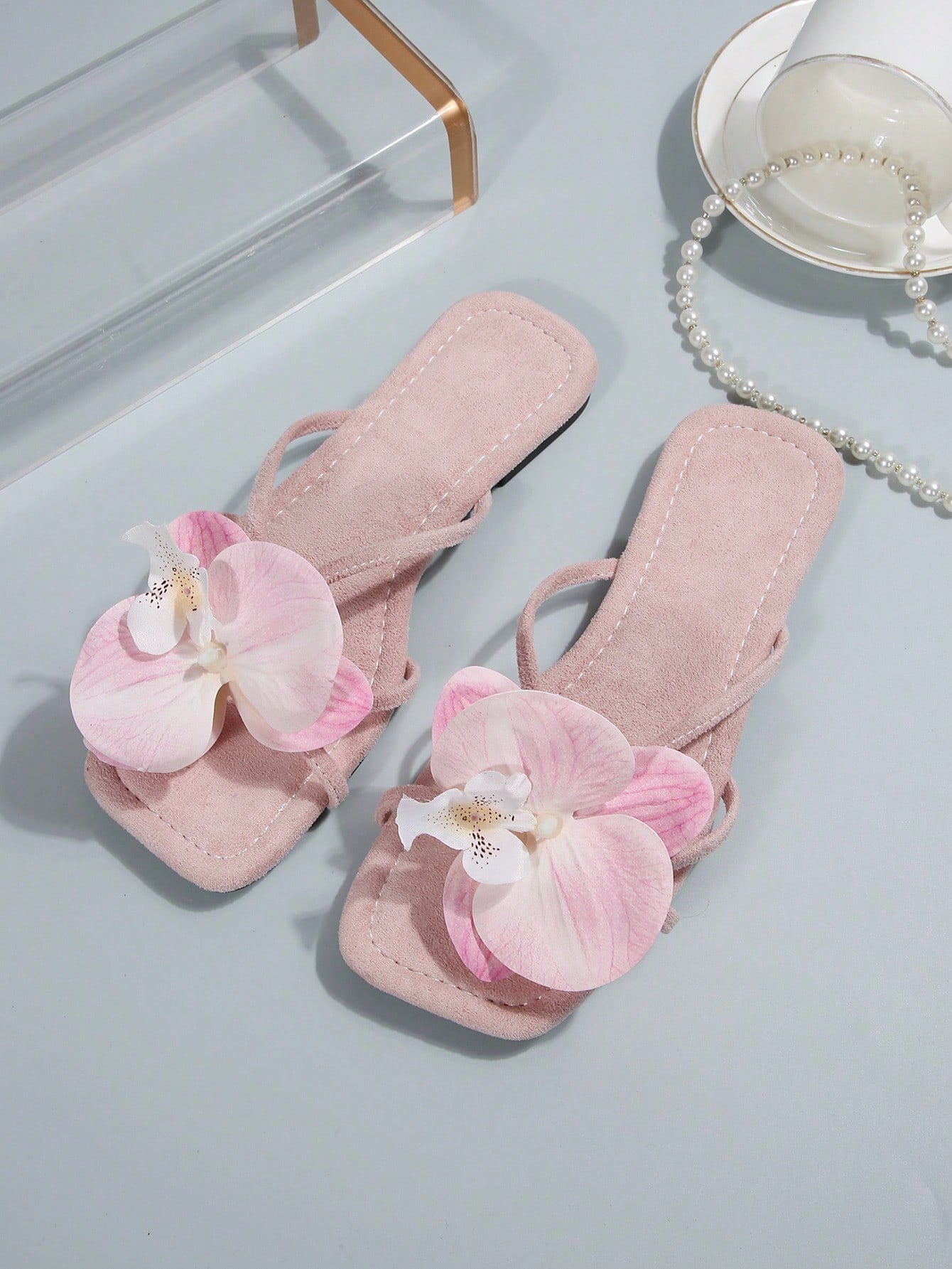 Women's flat slide sandals with open toe, floral applique detail, and criss-cross straps, shown as casual vacation-style summer footwear.