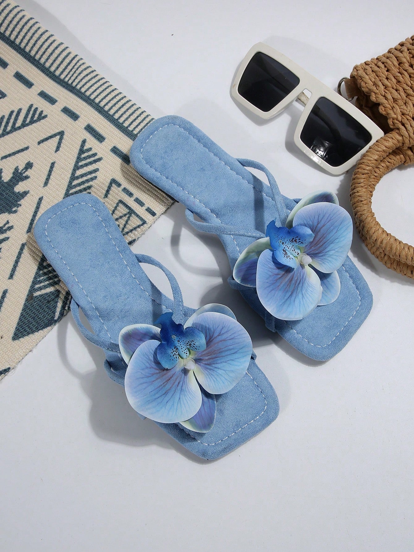 Women's flat slide sandals with open toe, floral applique detail, and criss-cross straps, shown as casual vacation-style summer footwear.