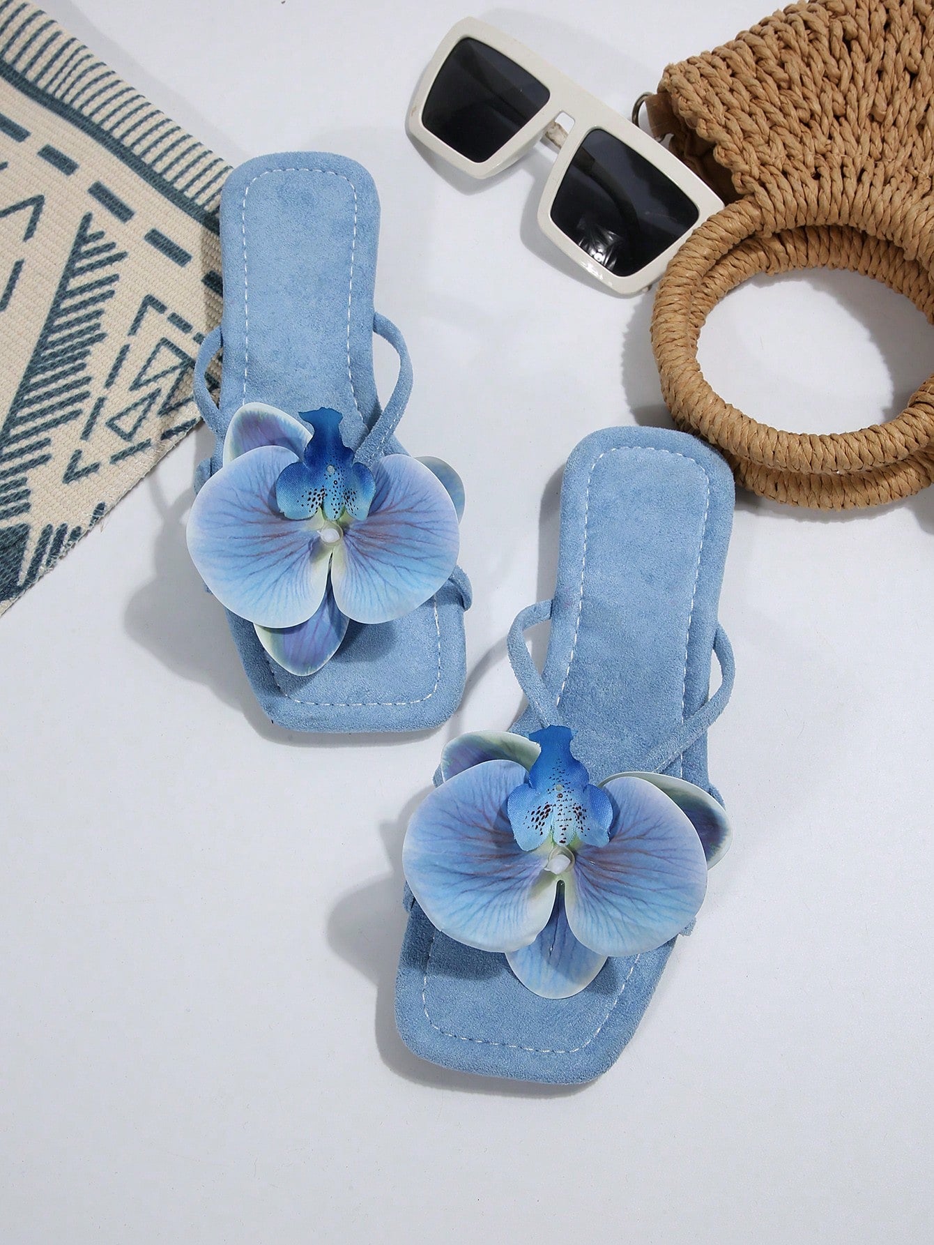 Women's flat slide sandals with open toe, floral applique detail, and criss-cross straps, shown as casual vacation-style summer footwear.