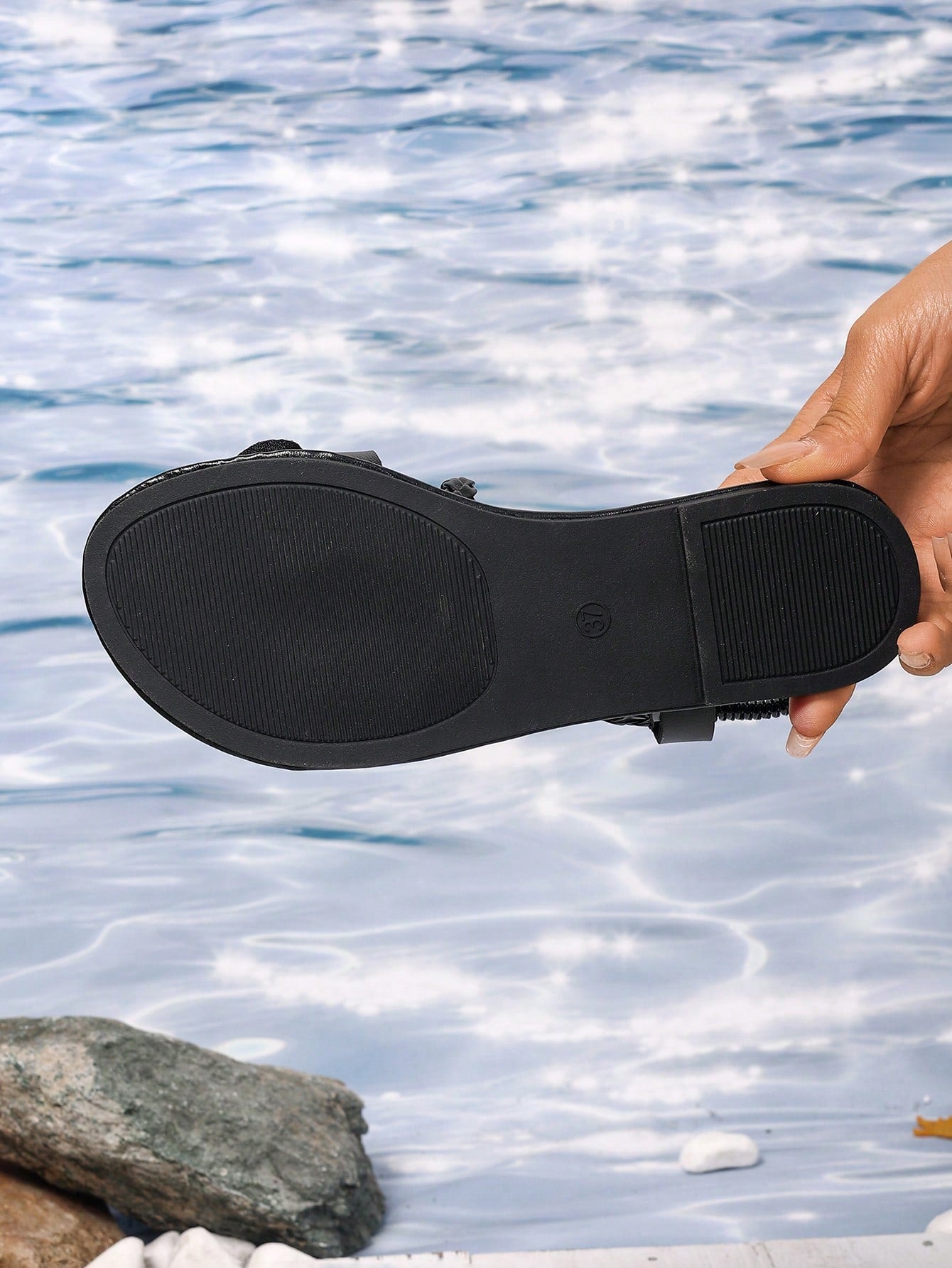 Women's open-toe flat slide sandals with crossed woven-look straps, floral appliqué detail, and buckle accent, shown in a casual beach style.