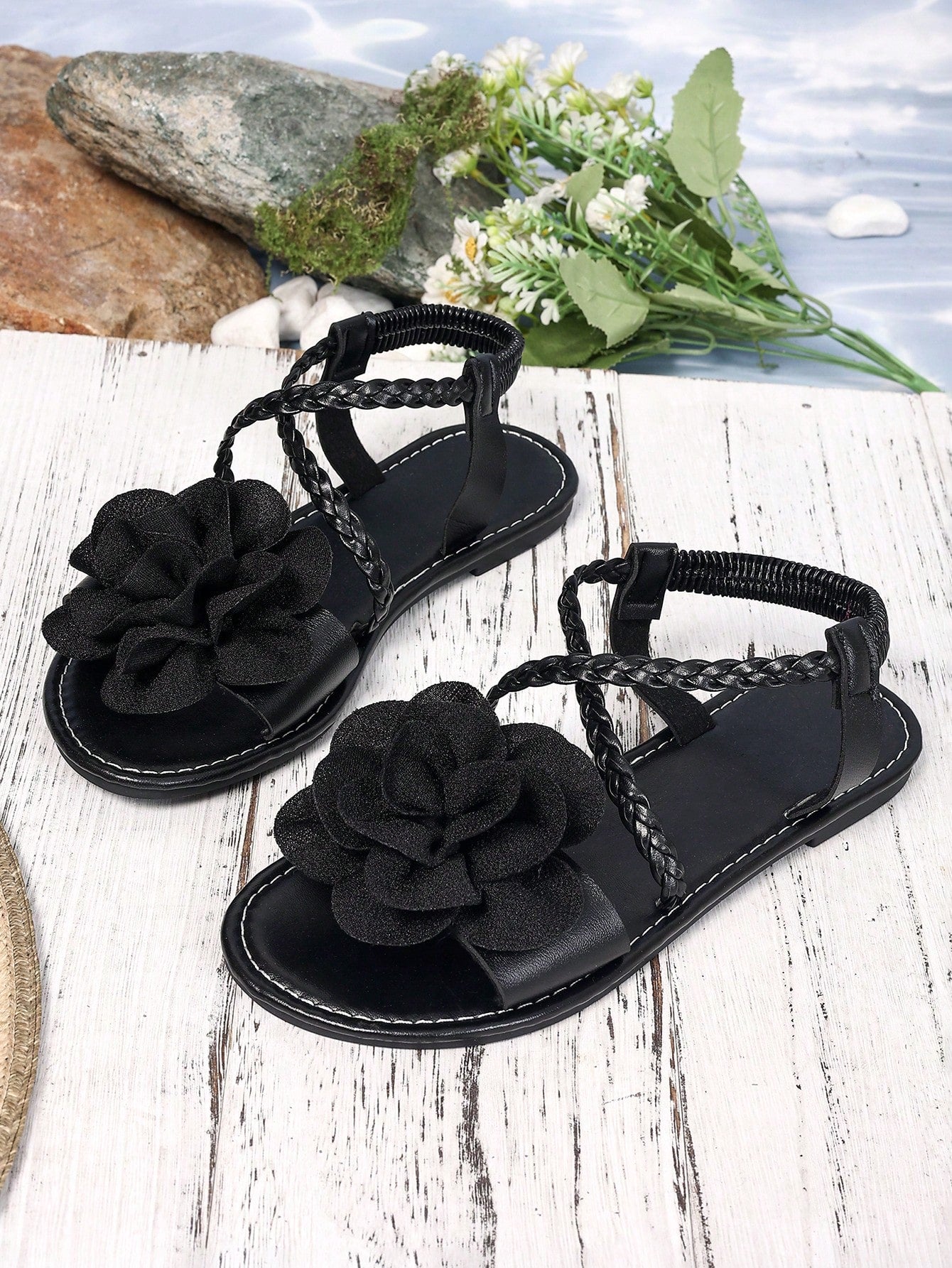 Women's open-toe flat slide sandals with crossed woven-look straps, floral appliqué detail, and buckle accent, shown in a casual beach style.