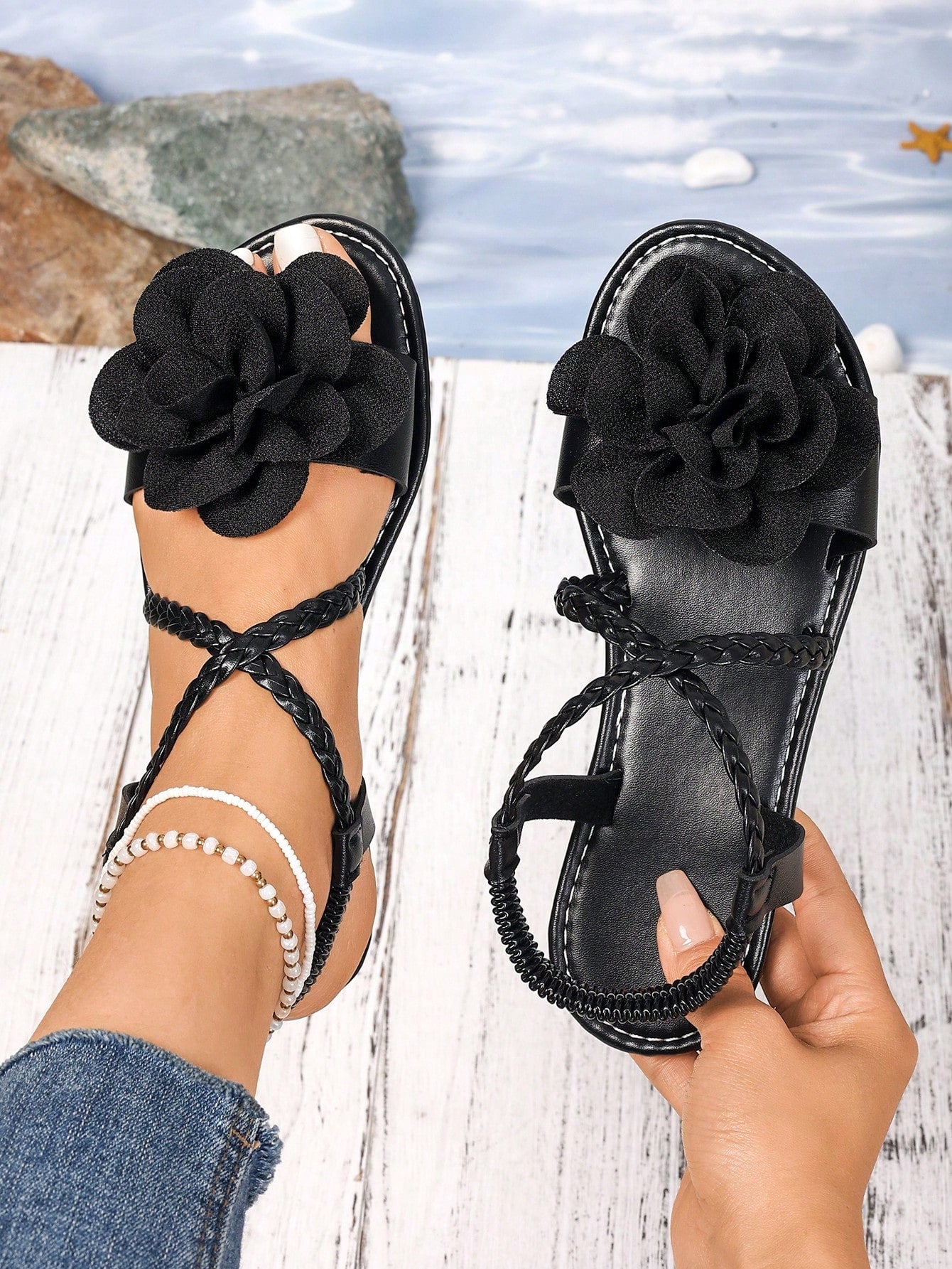 Women's open-toe flat slide sandals with crossed woven-look straps, floral appliqué detail, and buckle accent, shown in a casual beach style.