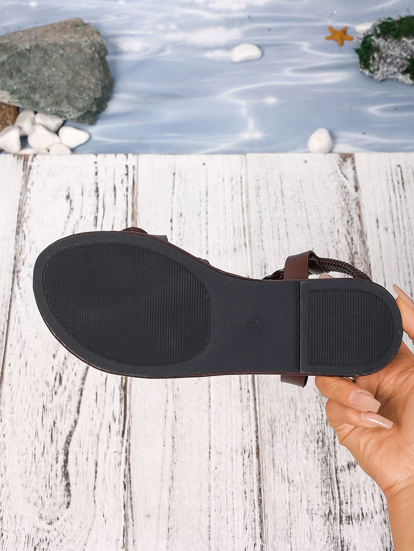 Women's open-toe flat slide sandals with crossed woven-look straps, floral appliqué detail, and buckle accent, shown in a casual beach style.