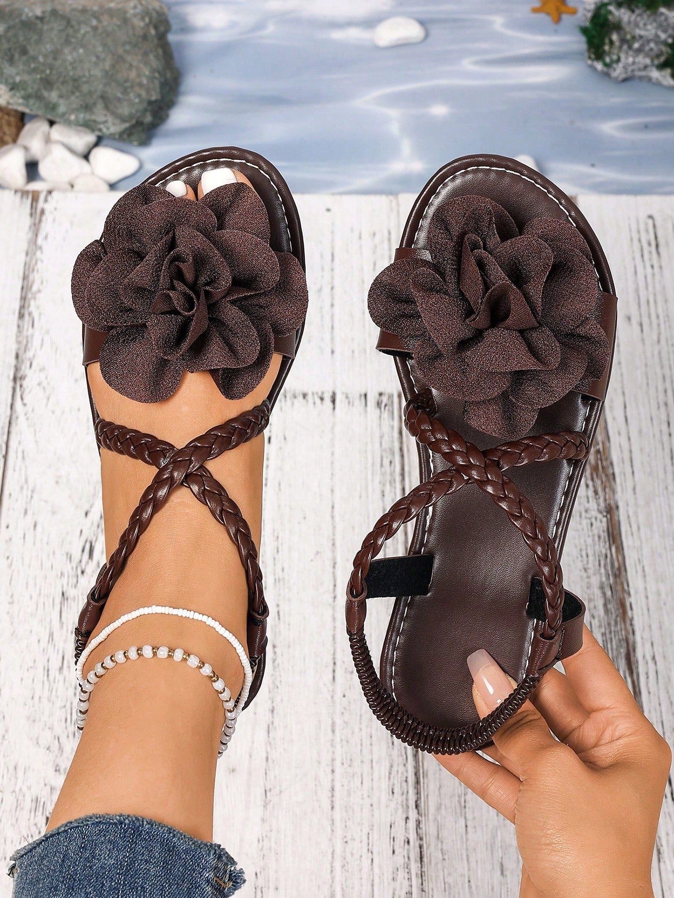 Women's open-toe flat slide sandals with crossed woven-look straps, floral appliqué detail, and buckle accent, shown in a casual beach style.