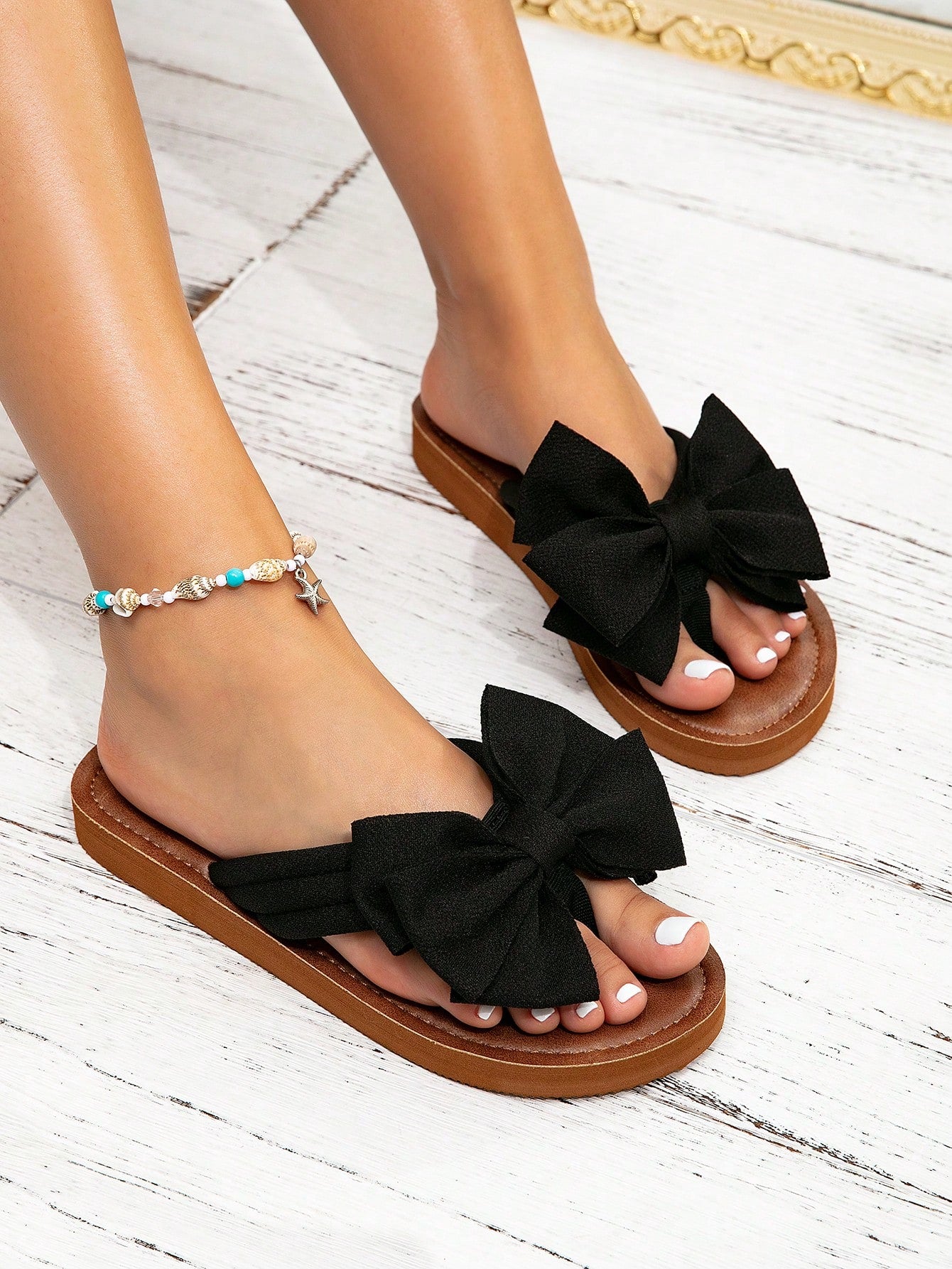 Women's flat slide sandals with ruched fabric, bow accent, and fringe detail, suitable for outdoor vacation wear.