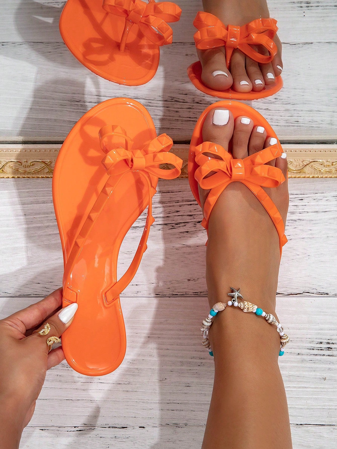 Pair of women's flat thong flip-flop sandals featuring bow decor and square stud accents, suitable for summer beach, resort, vacation, and everyday wear.