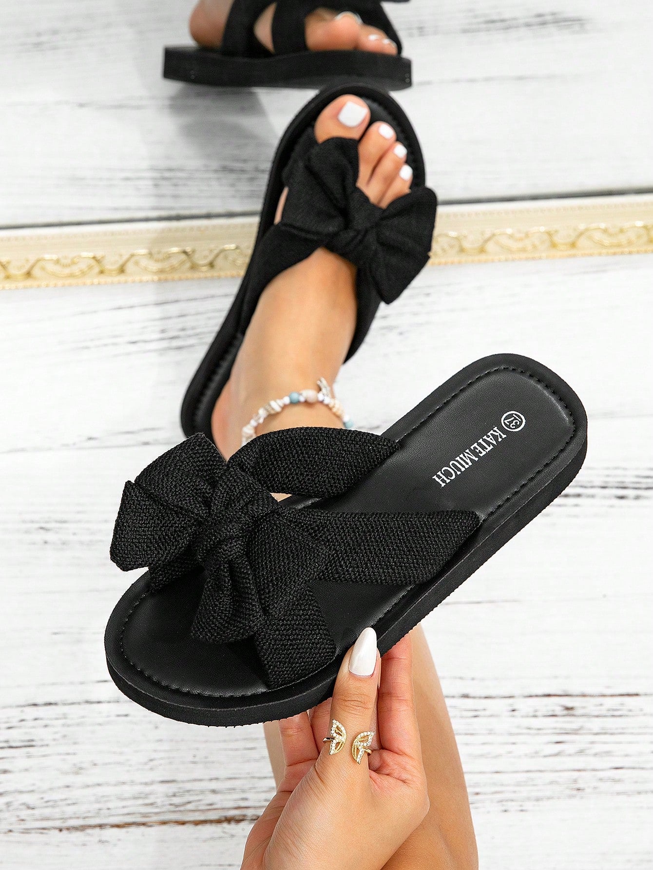 Women's flat slide sandals with ruched fabric, bow accent, and fringe detail, suitable for outdoor vacation wear.