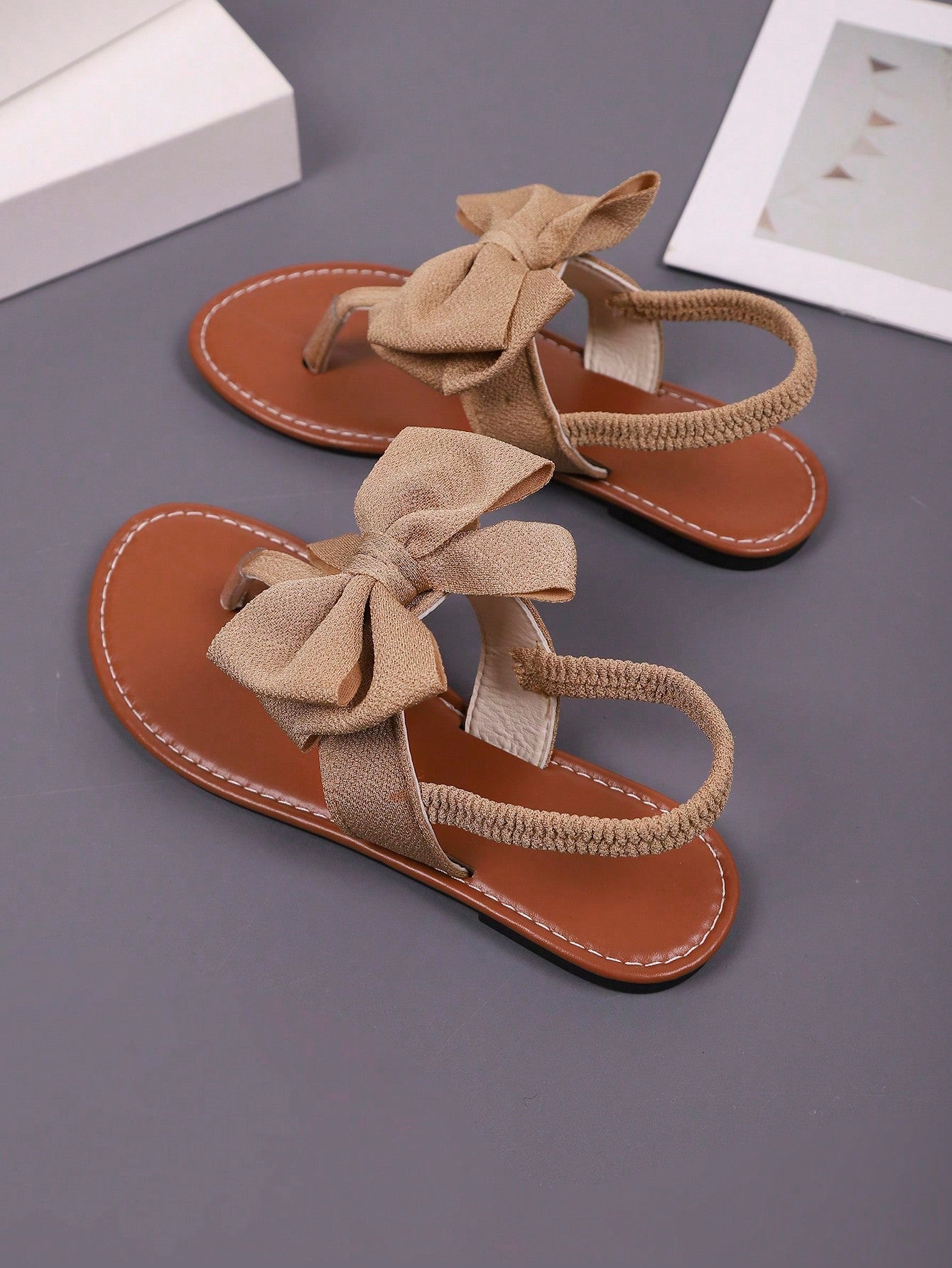 Pair of women’s solid color bohemian flat sandals with fabric bow detail, toe post thong design, and slide-on style for casual beach, outdoor, vacation, and home wear.