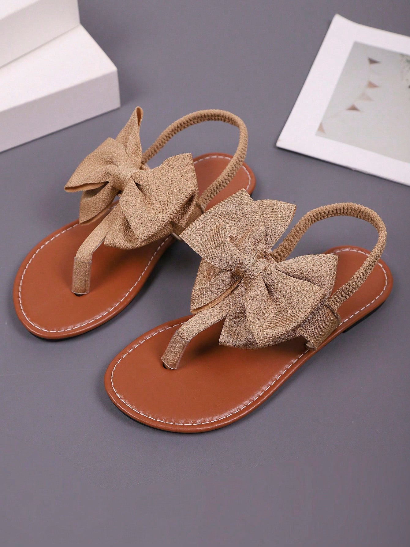 Pair of women’s solid color bohemian flat sandals with fabric bow detail, toe post thong design, and slide-on style for casual beach, outdoor, vacation, and home wear.
