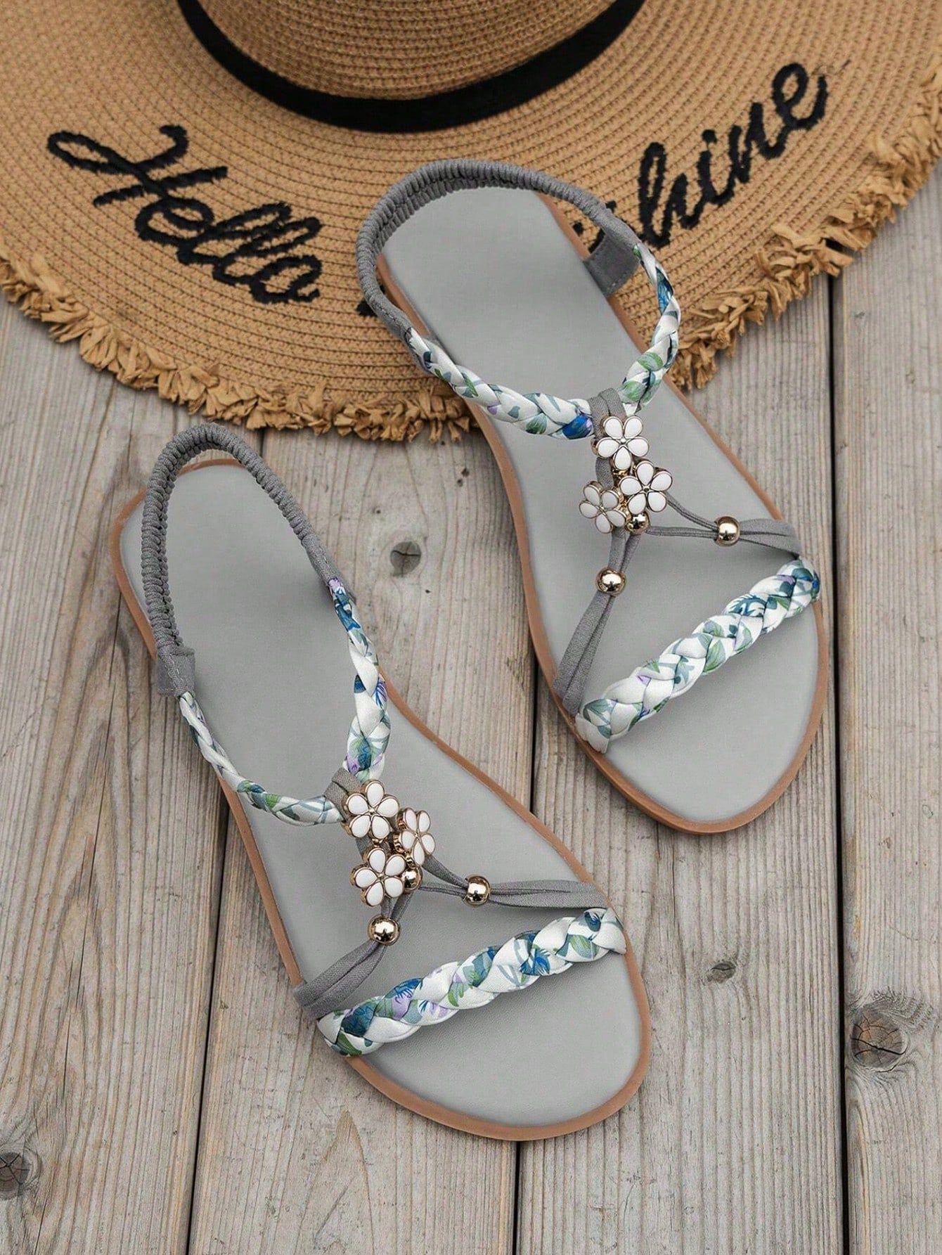 Pair of women’s flat gladiator sandals with woven fabric straps, ruched detailing, open toes, and decorative buckle and floral accents.