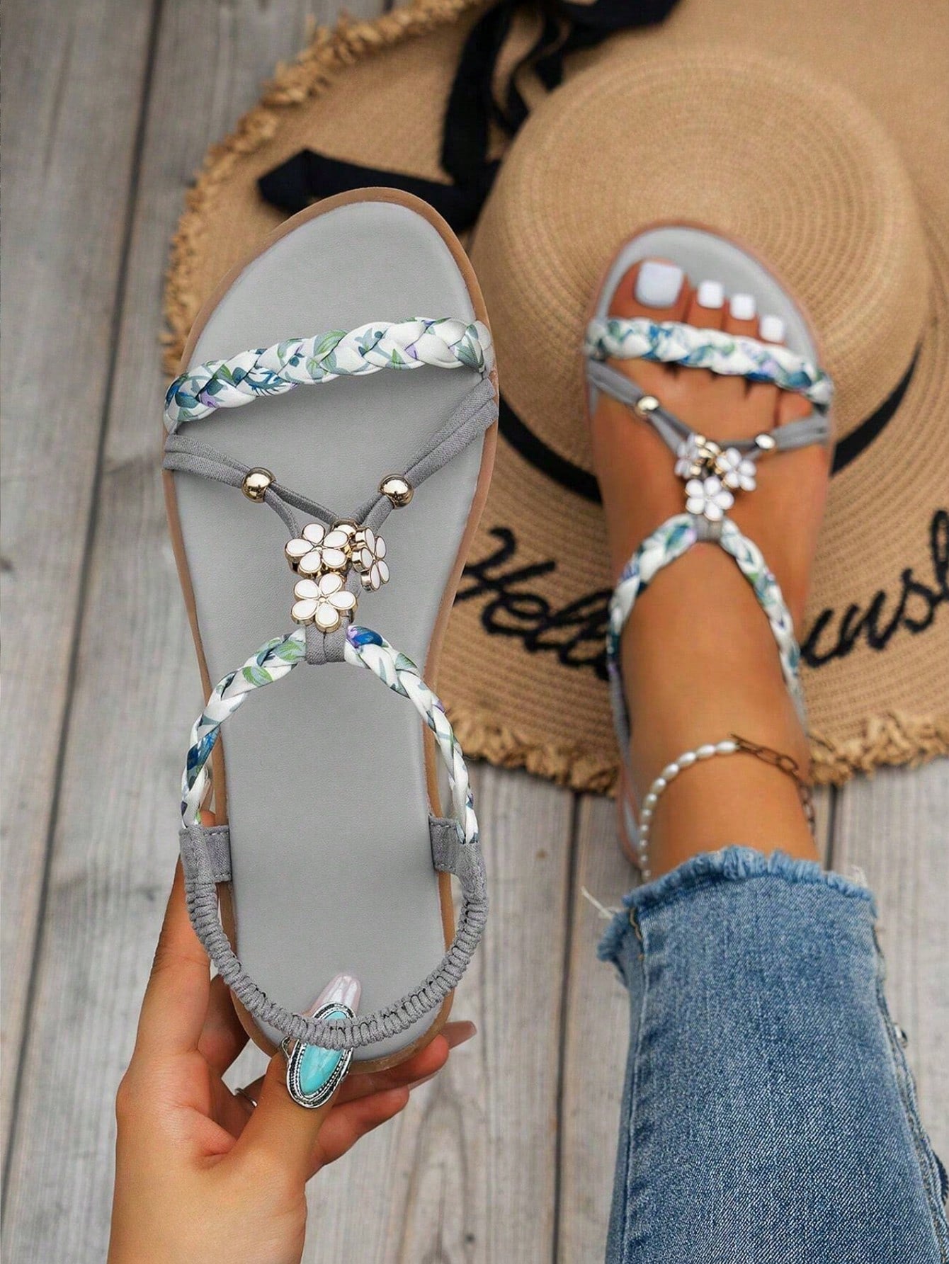 Pair of women’s flat gladiator sandals with woven fabric straps, ruched detailing, open toes, and decorative buckle and floral accents.