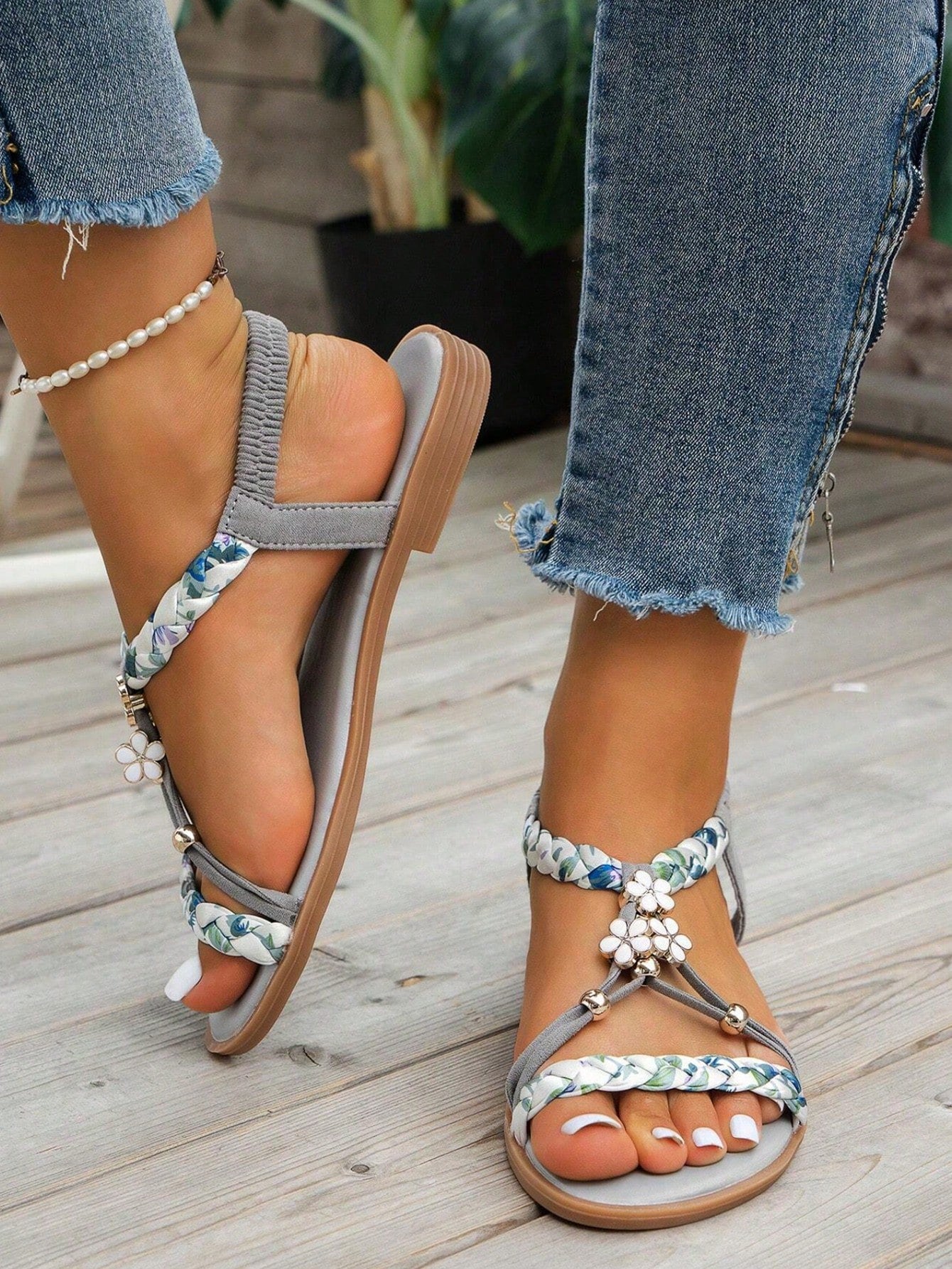 Pair of women’s flat gladiator sandals with woven fabric straps, ruched detailing, open toes, and decorative buckle and floral accents.