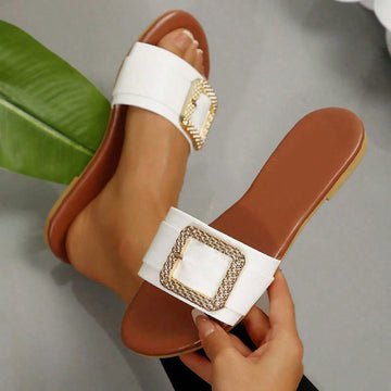 Women’s wide fit white flat slide mules with draped strap detail, square buckle accent, and open toe design, suitable for summer daily wear, vacation, and outdoor activities.