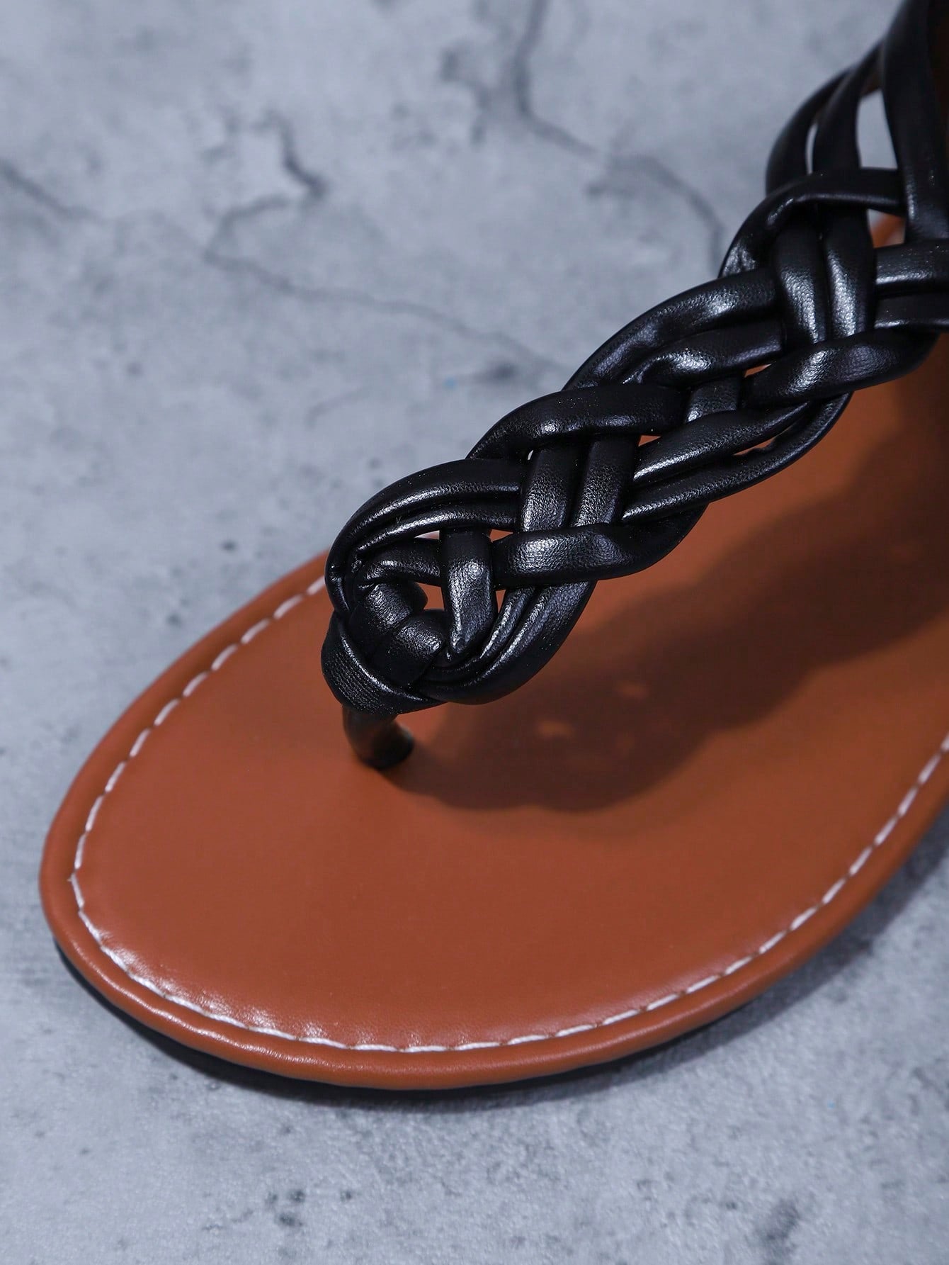 Women's black handmade woven flat thong gladiator sandals with braided criss-cross straps, toe post design, and flat rubber sole.