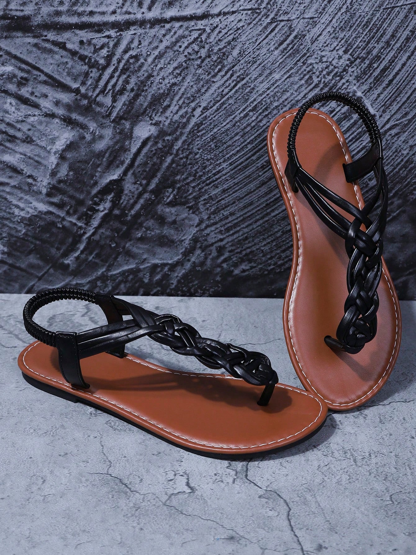 Women's black handmade woven flat thong gladiator sandals with braided criss-cross straps, toe post design, and flat rubber sole.
