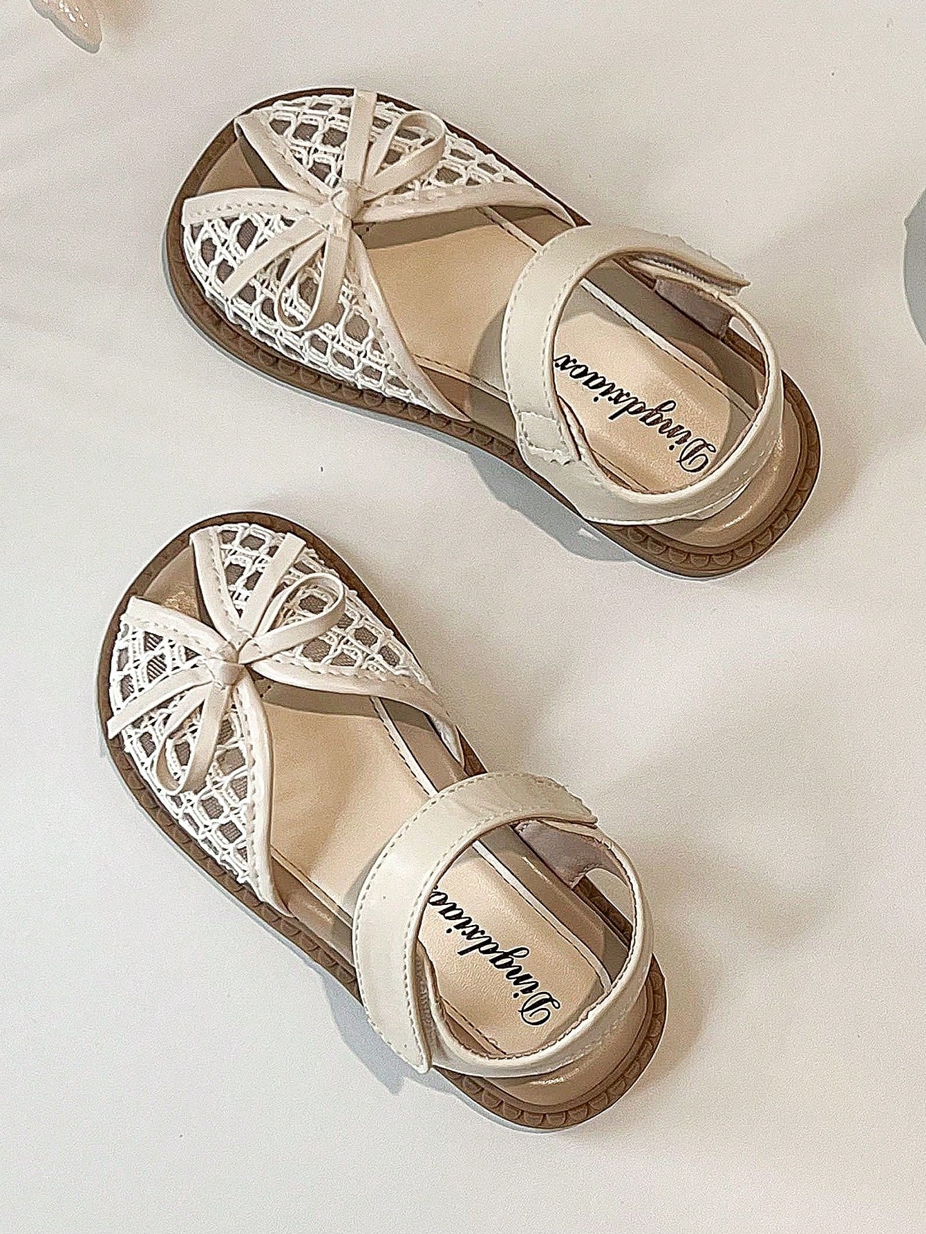 Pair of girls' pink open-toe flat sandals with ankle straps, buckle details, and a non-slip black rubber outsole.