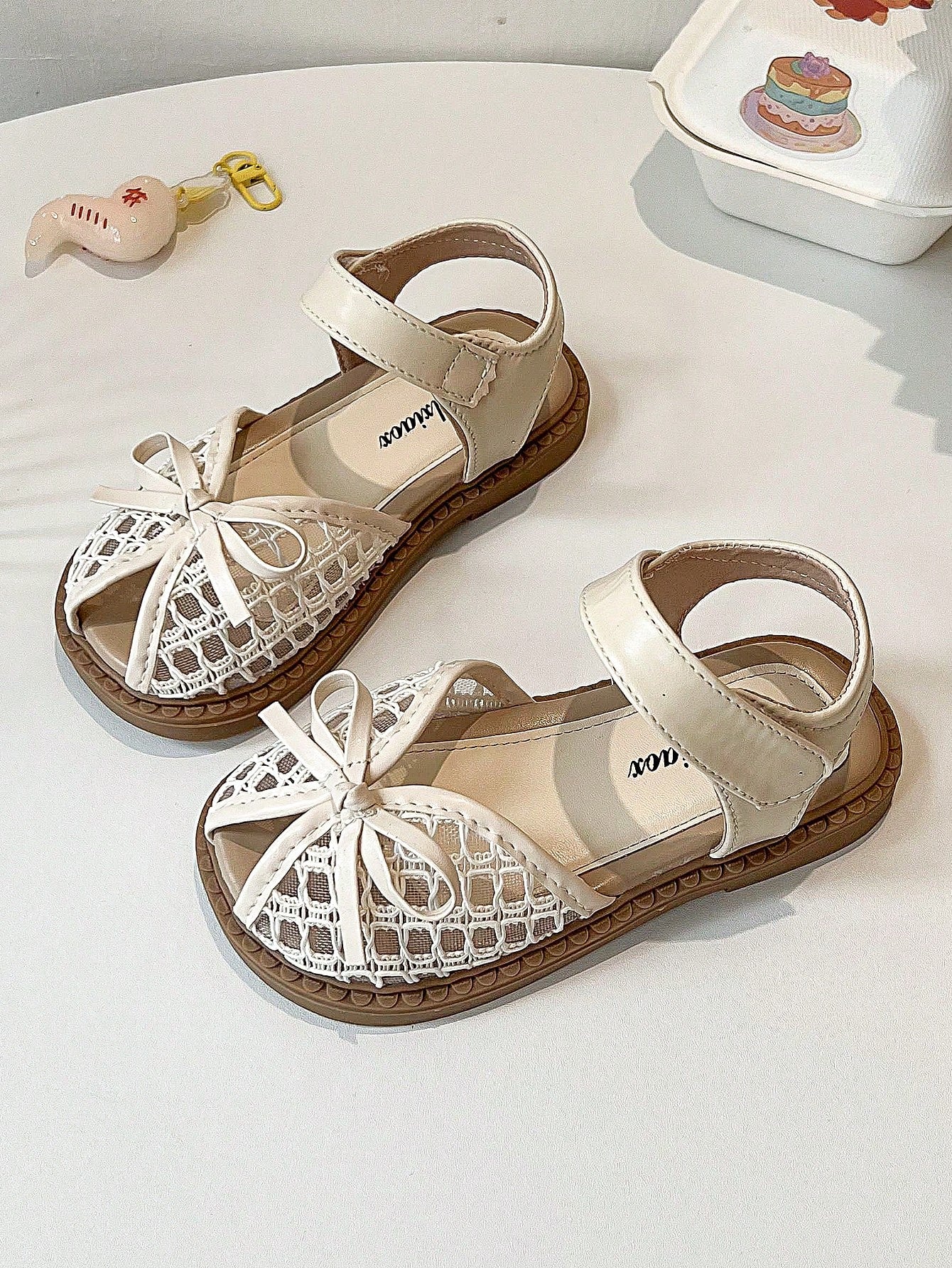Pair of girls' pink open-toe flat sandals with ankle straps, buckle details, and a non-slip black rubber outsole.