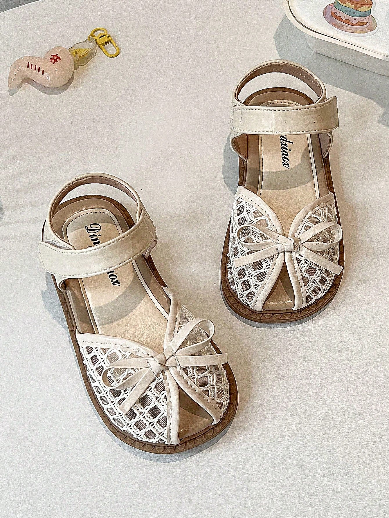 Pair of girls' pink open-toe flat sandals with ankle straps, buckle details, and a non-slip black rubber outsole.